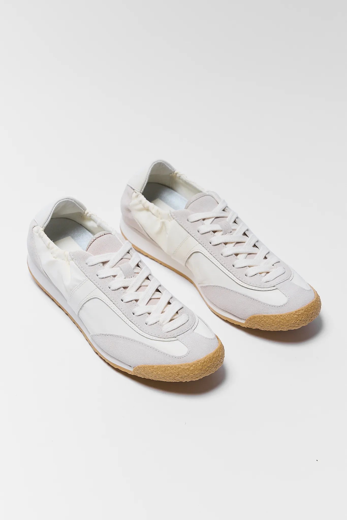 two white sneakers with tan soles on white background