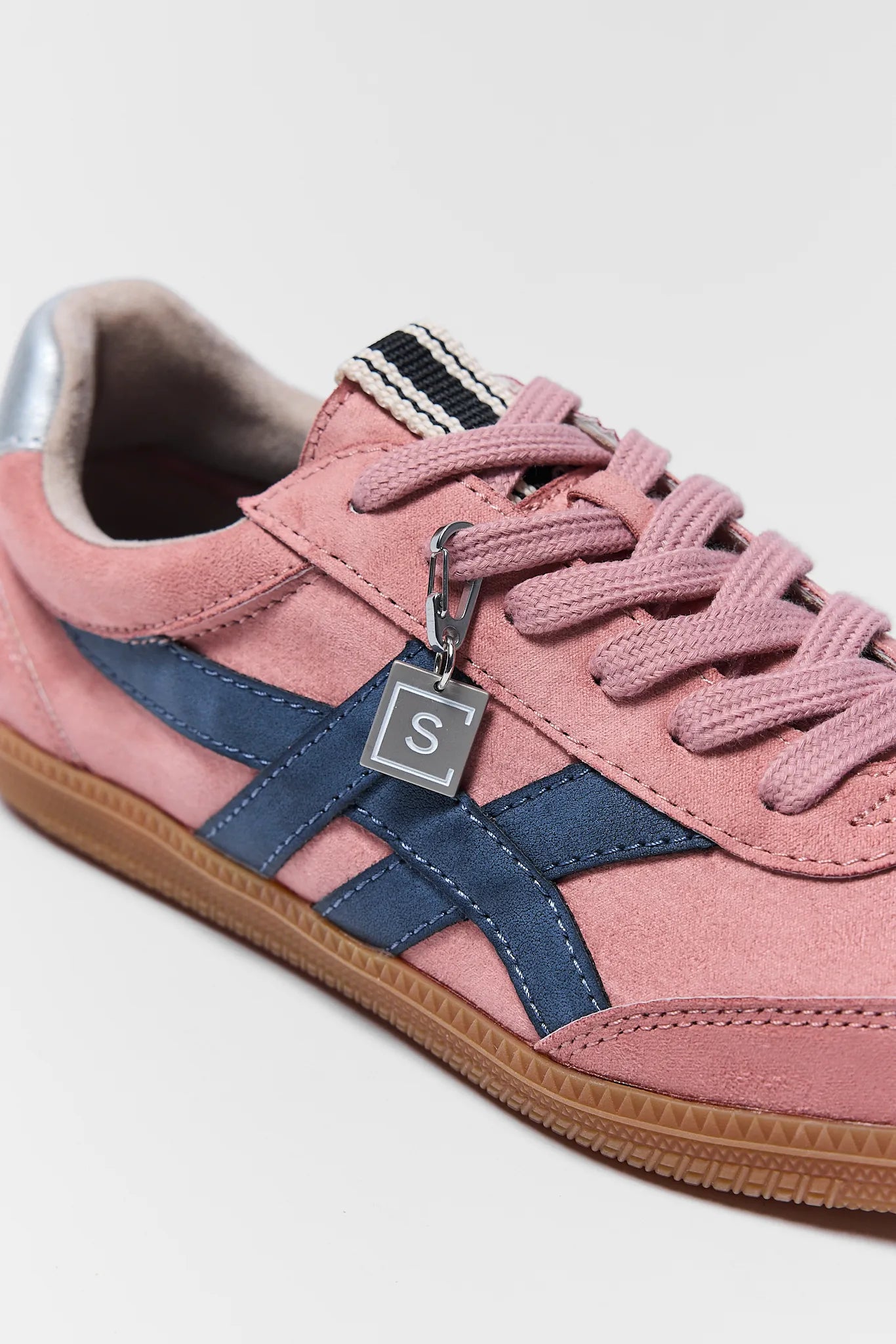 pink sneakers with navy details and silver charm on white background