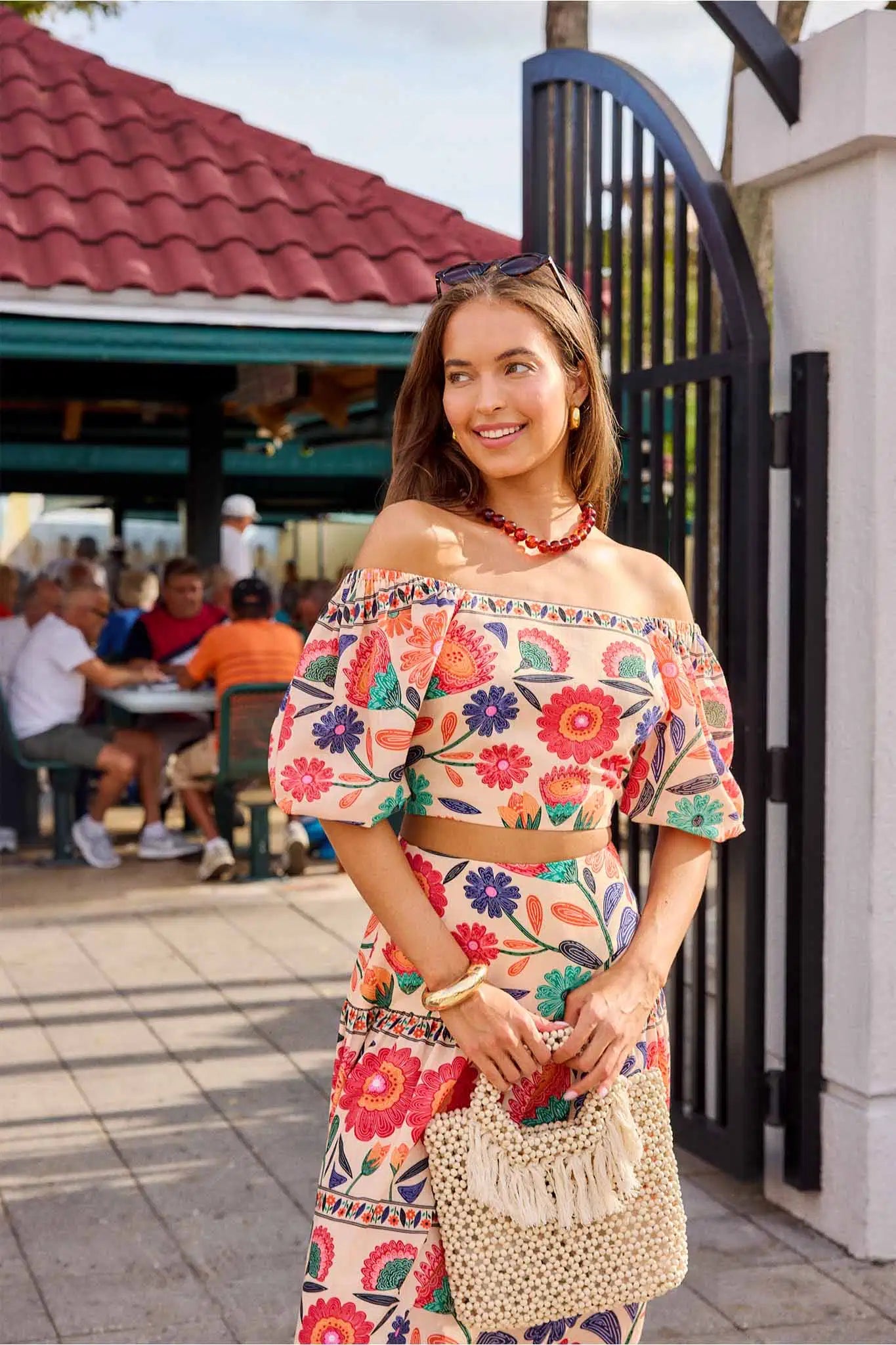 Woman in a colorful floral outfit standing outdoors with a casual setting in the background.
