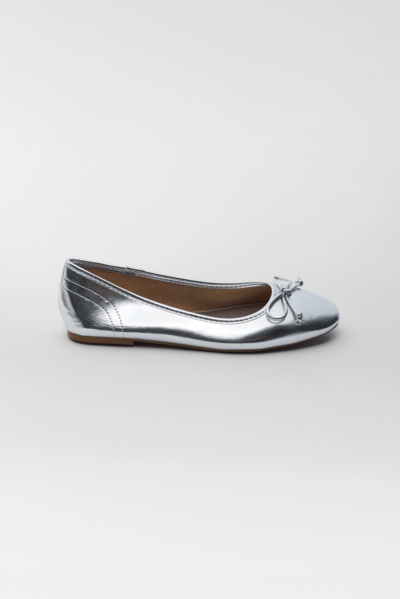 A single metallic silver ballet flat shoe with a small bow detail on the toe, shown in profile against a light gray background.