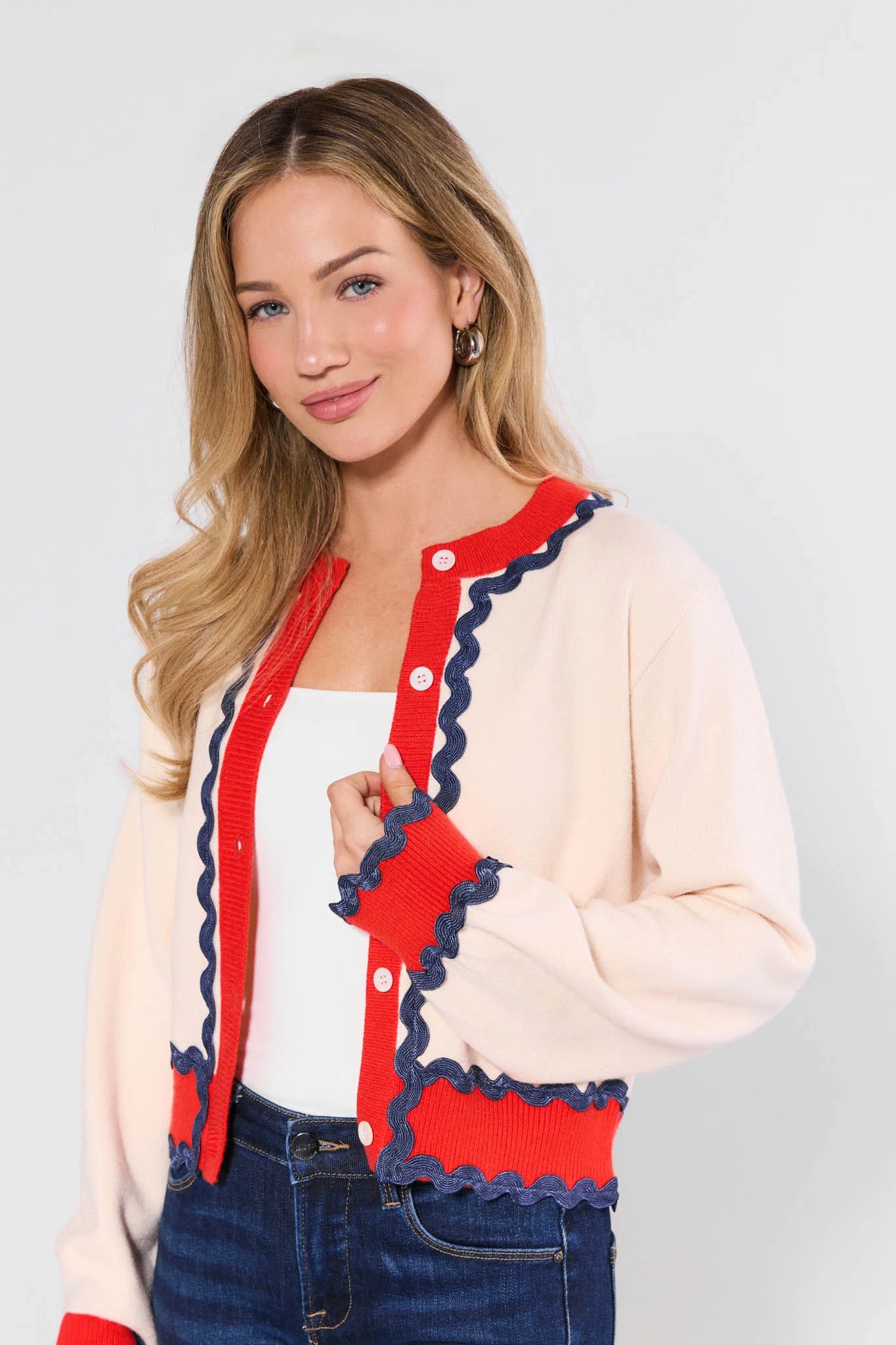 Woman wearing a cream cardigan with red and blue trim on a white background