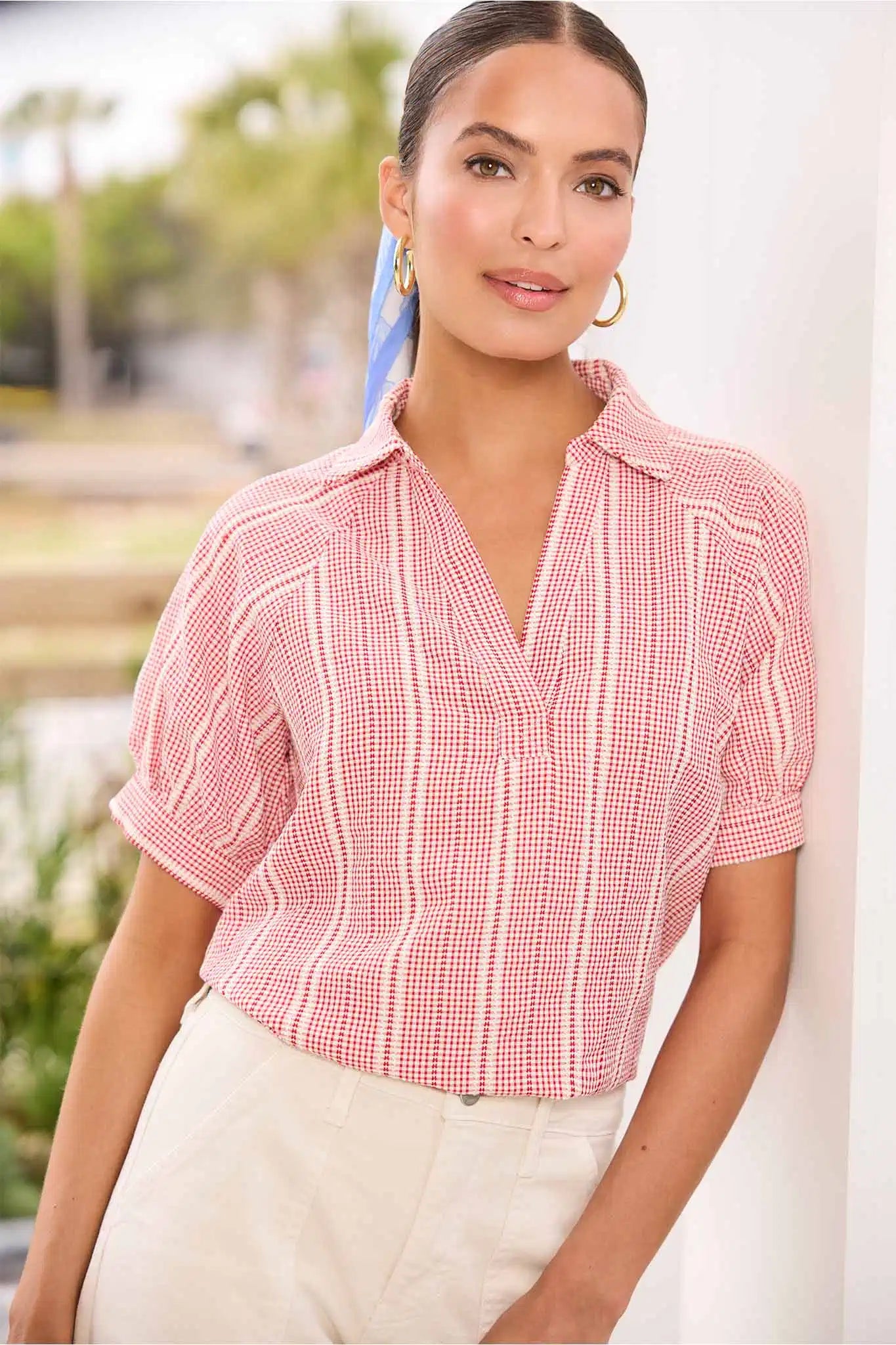 Woman wearing a red and white checkered blouse with a blurred outdoor background