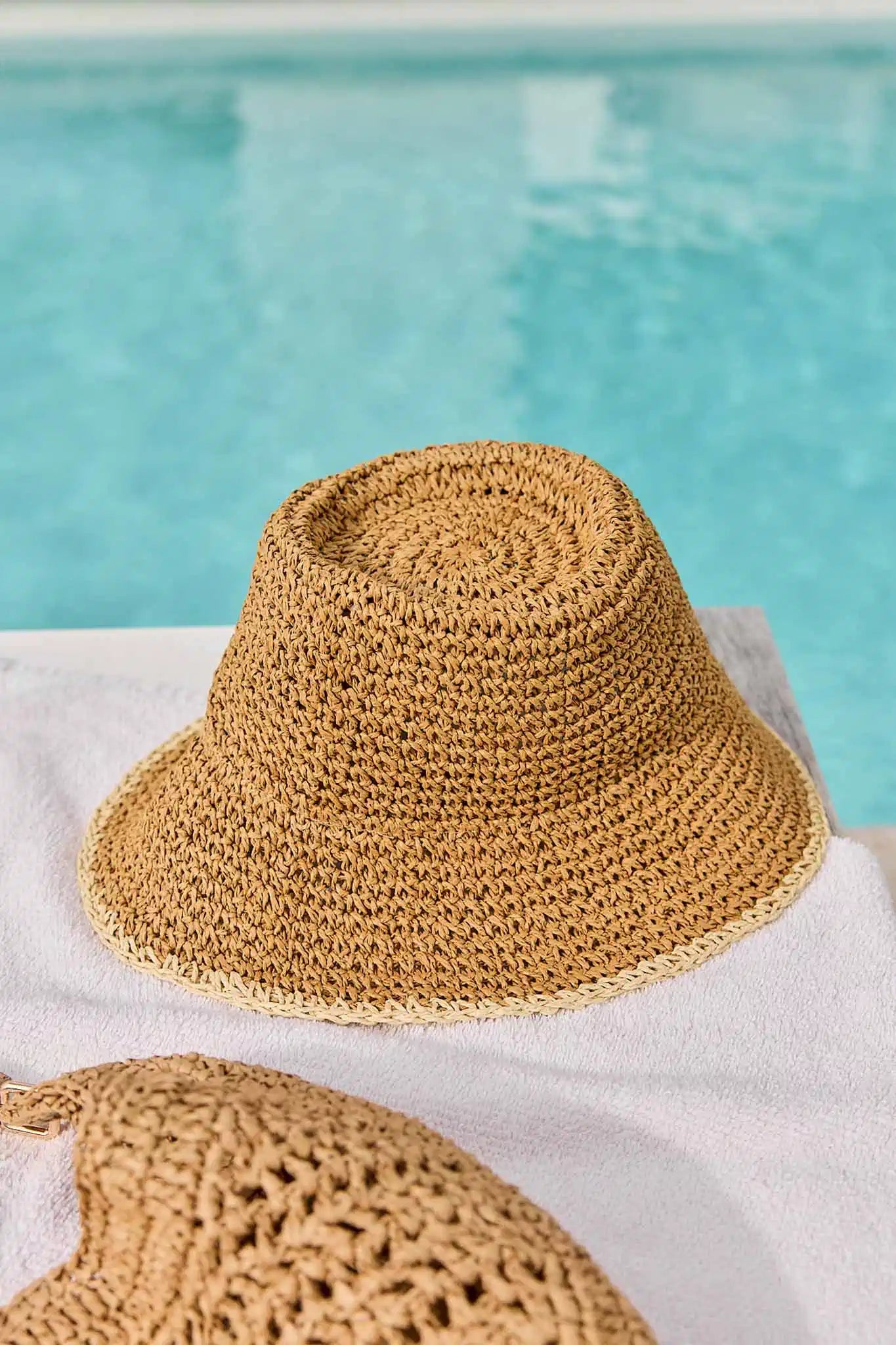 Woven straw hat on a white towel by a pool