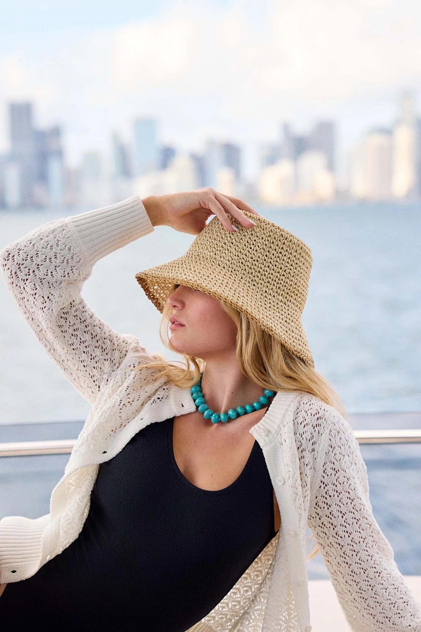 Woman wearing a straw hat and white cardigan with a city skyline in the background