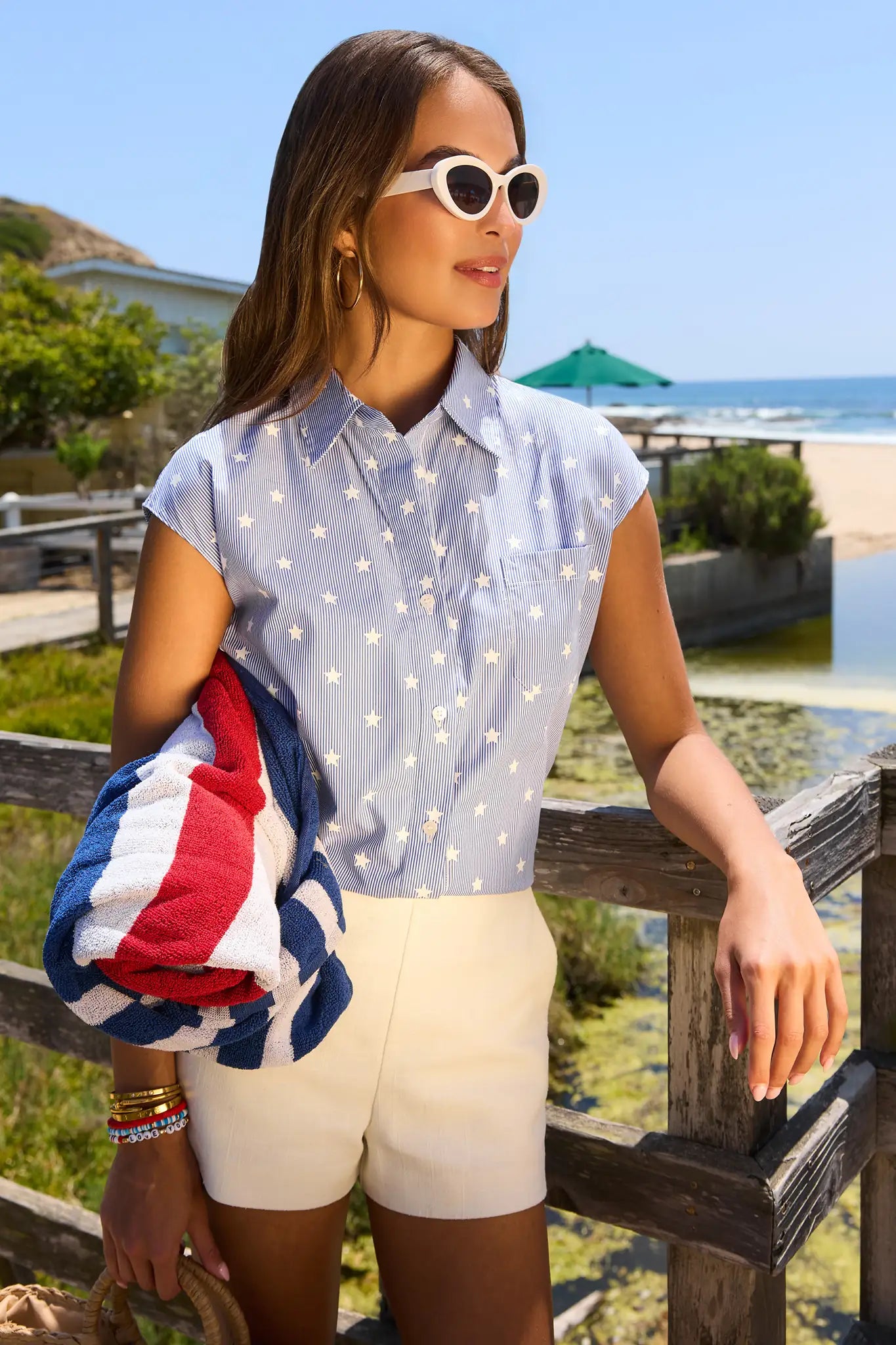 Woman in a light blue shirt and white shorts holding a flag by a waterfront. flag