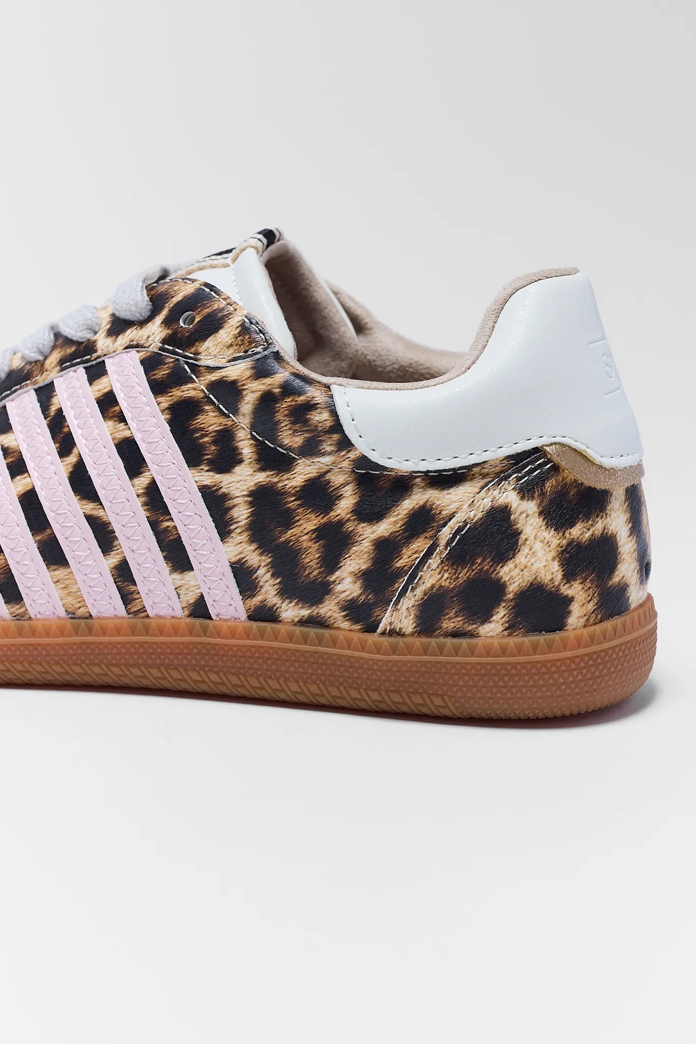 A low-top sneaker featuring a leopard print pattern on the upper, white leather side stripes, a white heel tab, and a brown gum sole, shown against a plain light gray background.