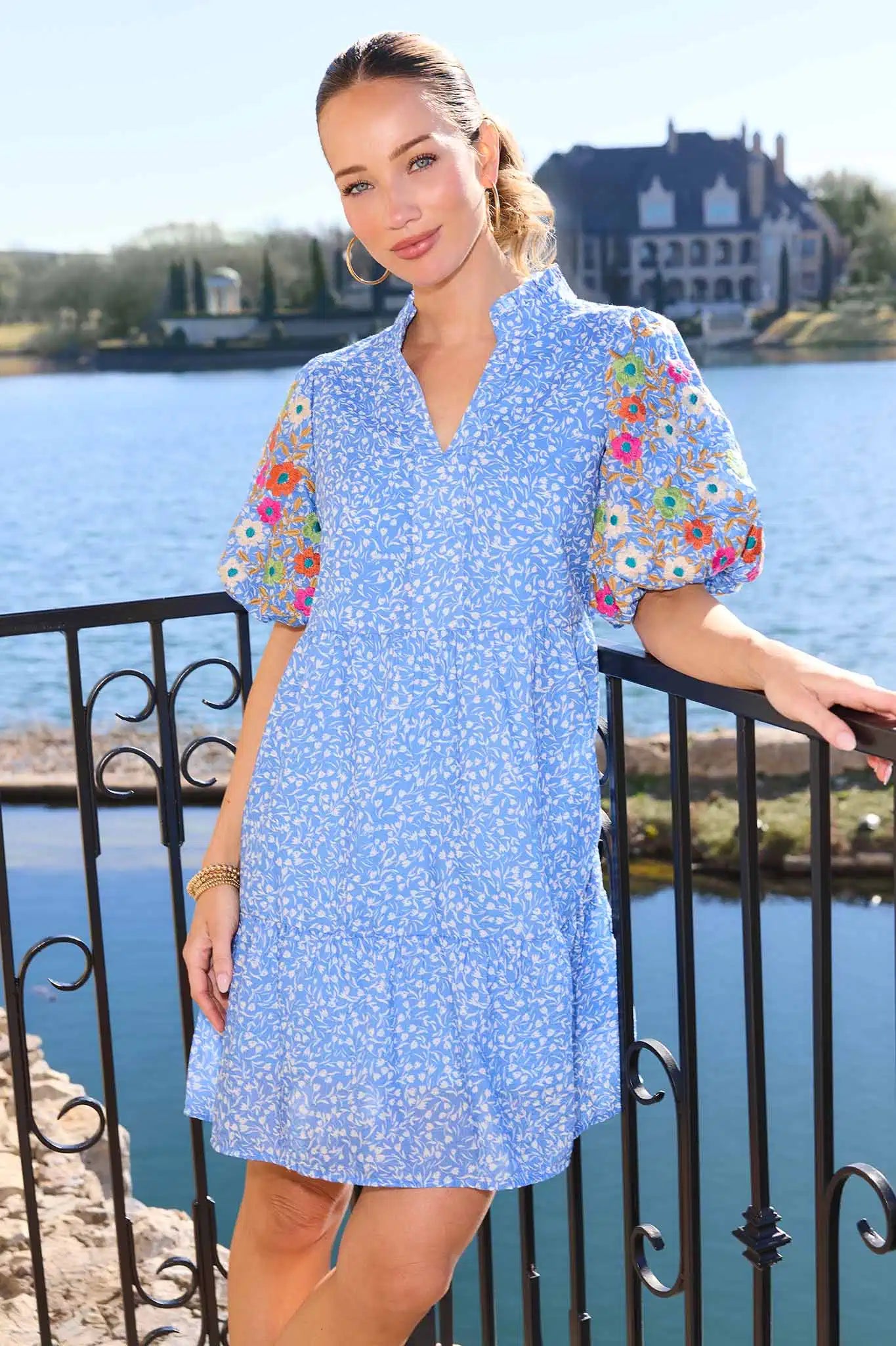 Woman in a blue dress with floral sleeves by a waterfront.
