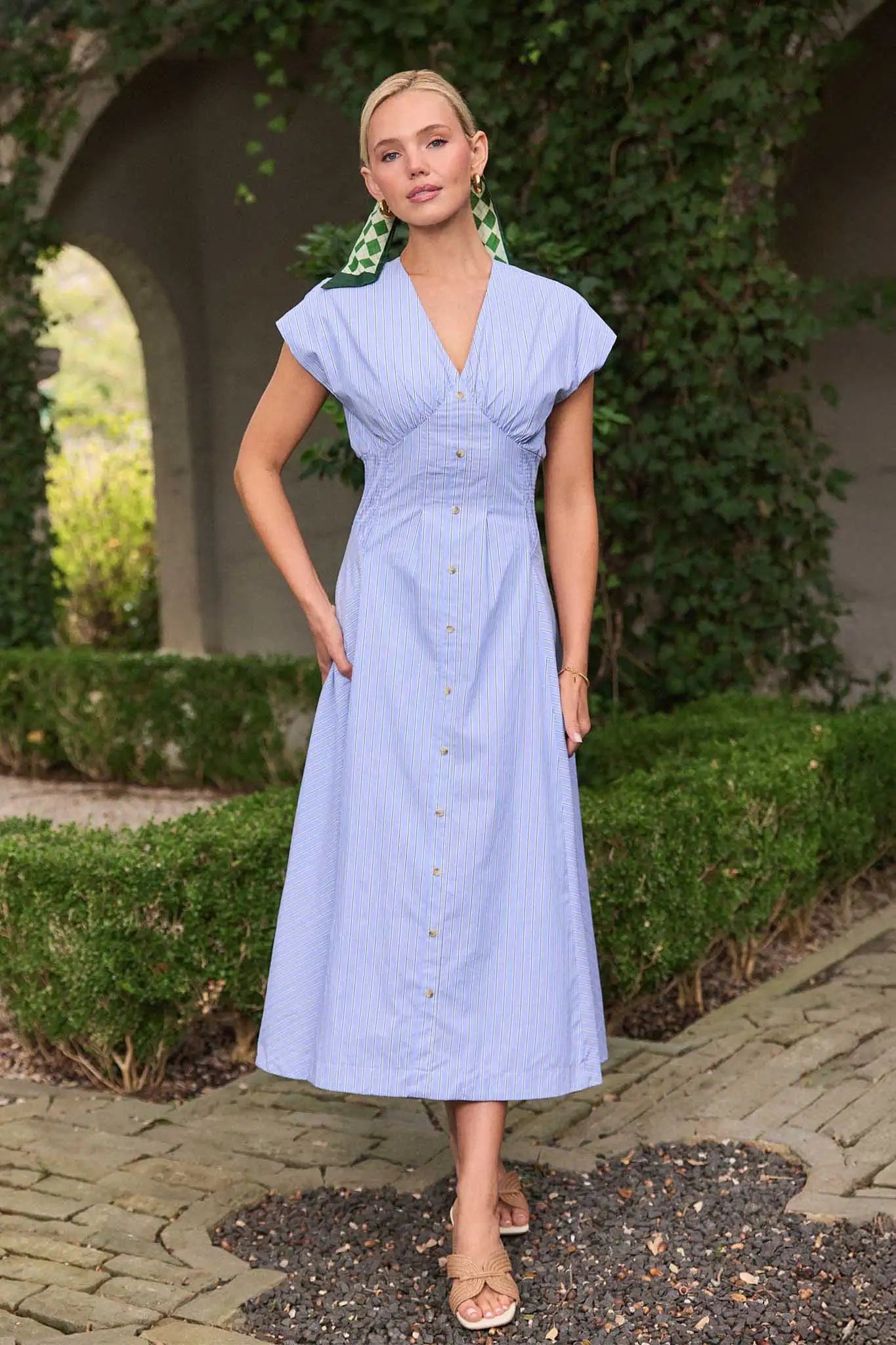Woman in a light blue dress standing outdoors with greenery in the background