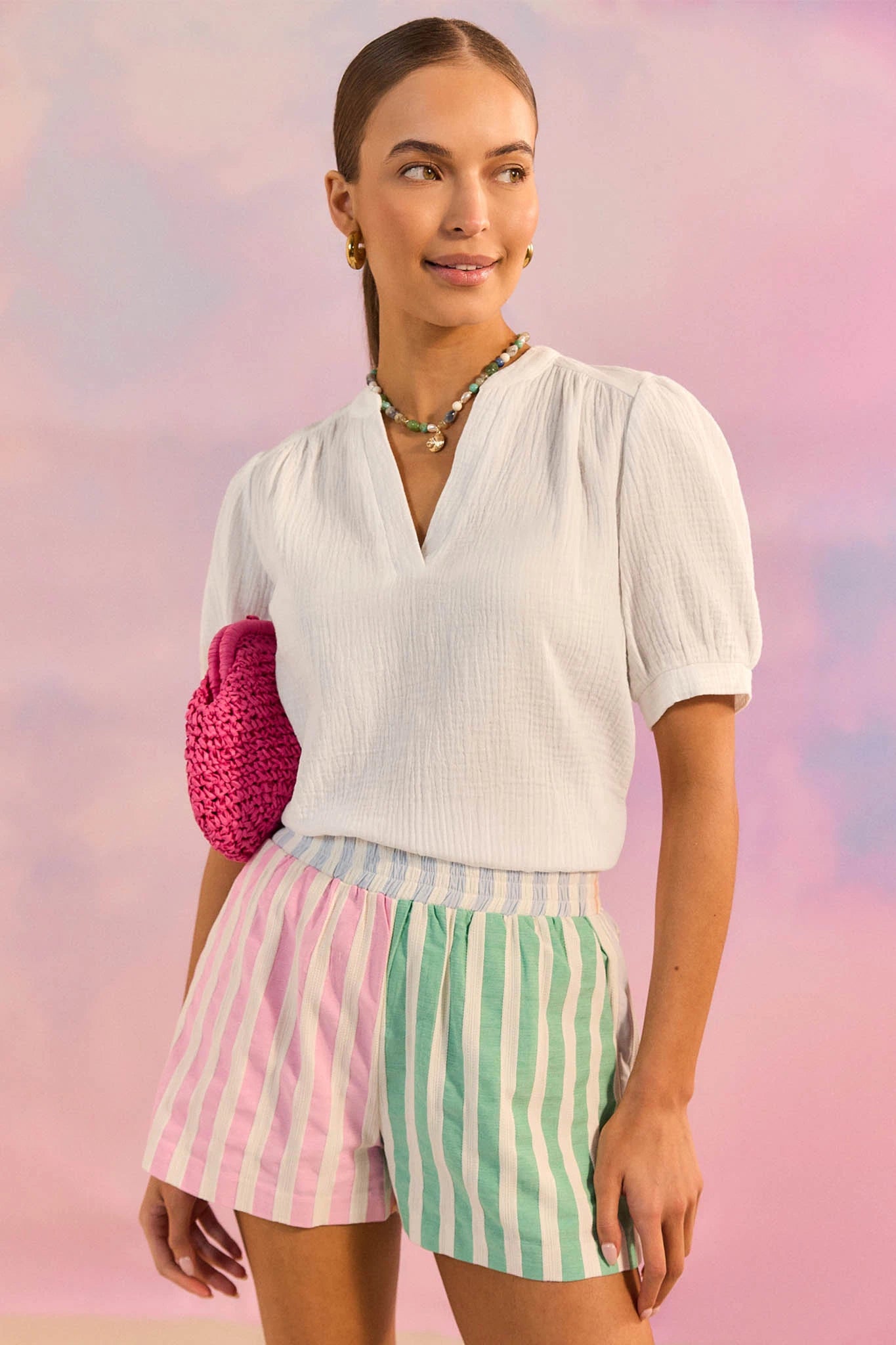 Woman wearing a white blouse and colorful shorts against a pastel background