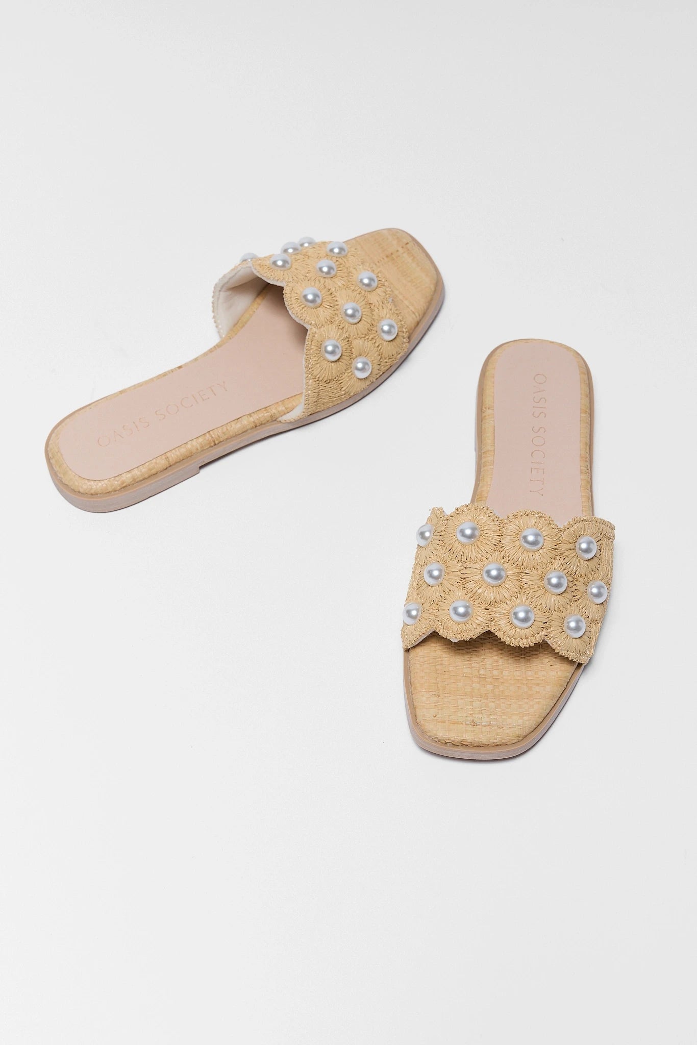 Pair of beige sandals with pearl embellishments on a light gray background