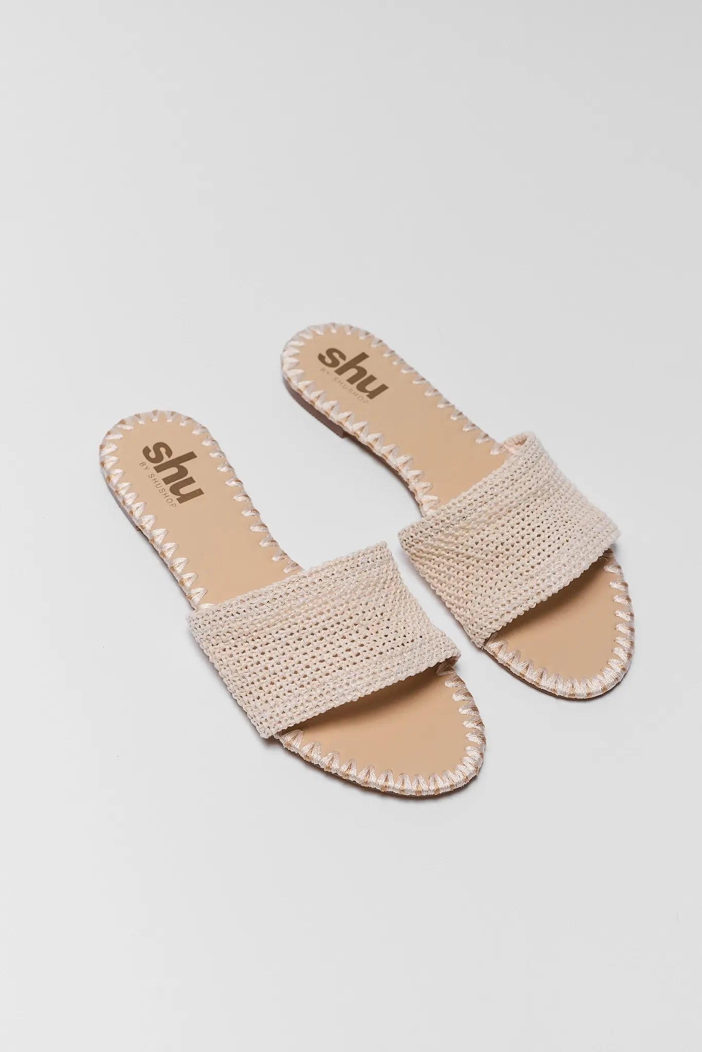 Pair of beige sandals with 'shu' branding on a light gray background