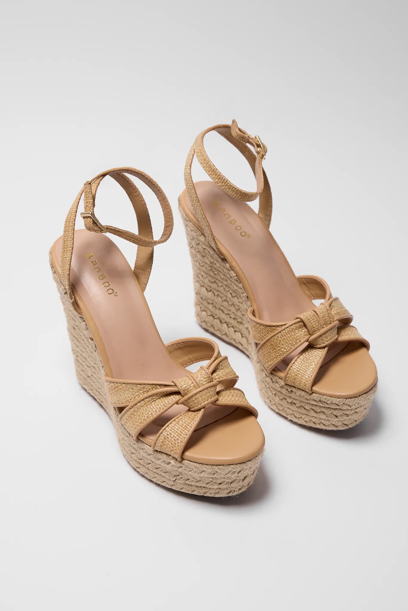 Pair of tan wedge sandals with espadrille sole on a gray background