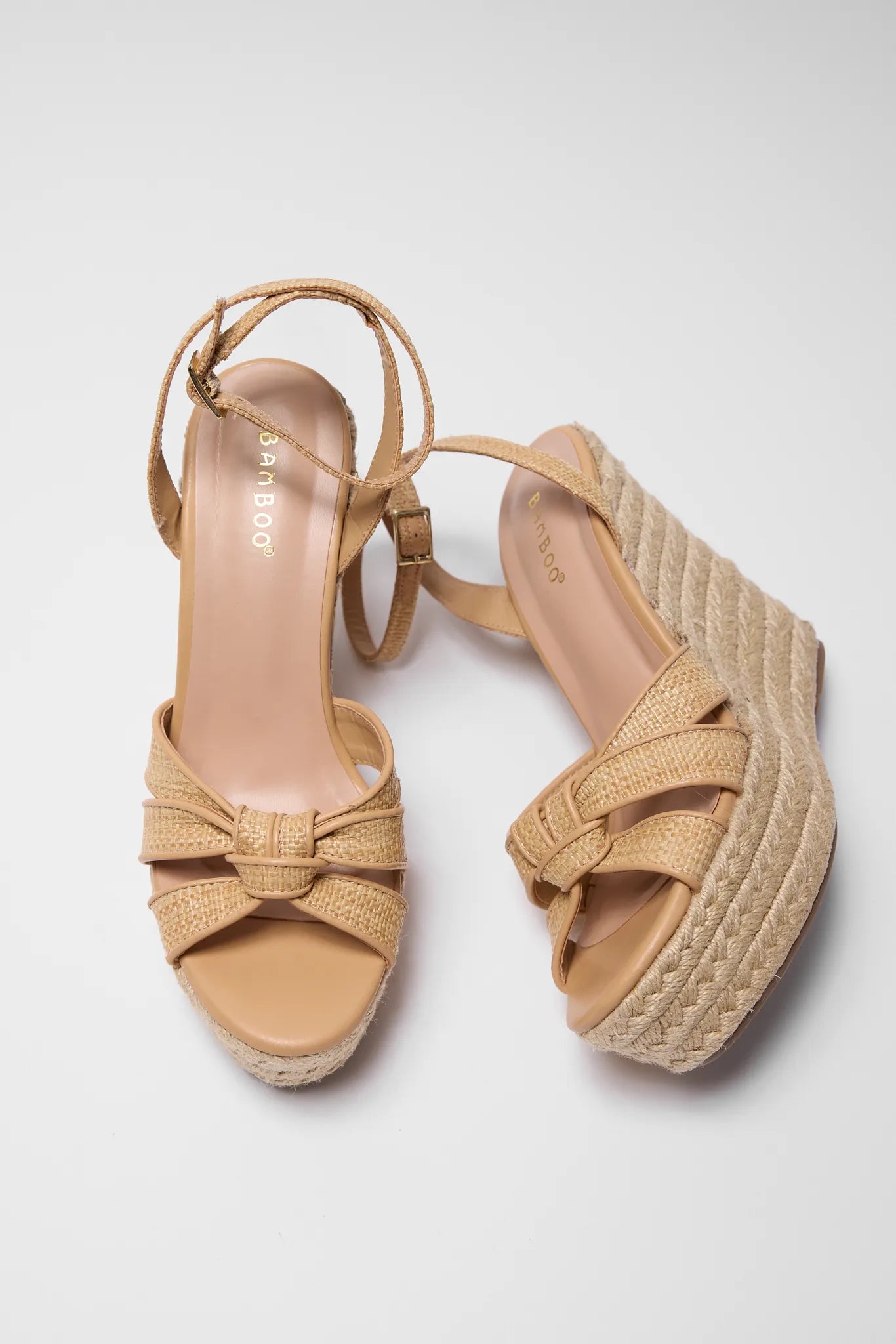 Pair of tan wedge sandals with woven platform sole on a light gray background