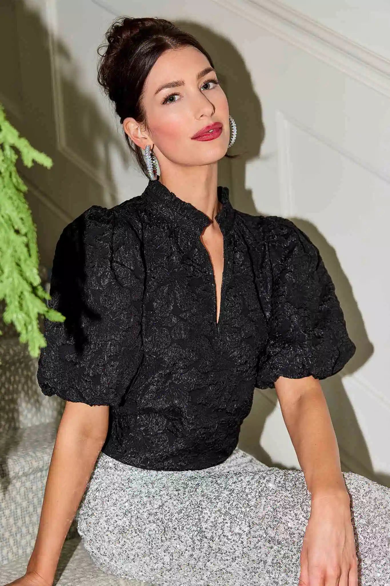 Woman wearing a black Teresa top with puffed sleeves and a silver skirt.