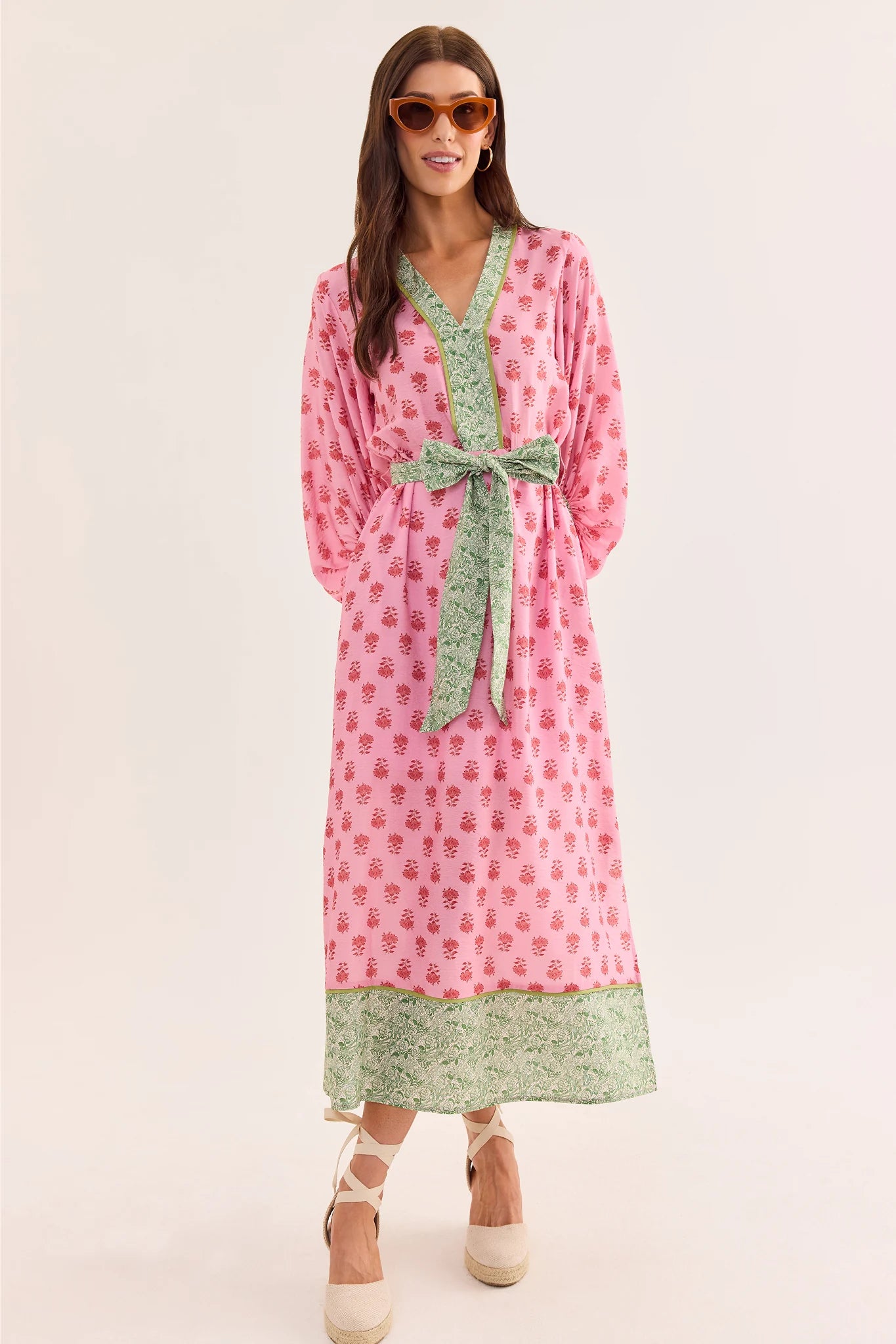Woman wearing a pink and green patterned dress with a belt on a white background