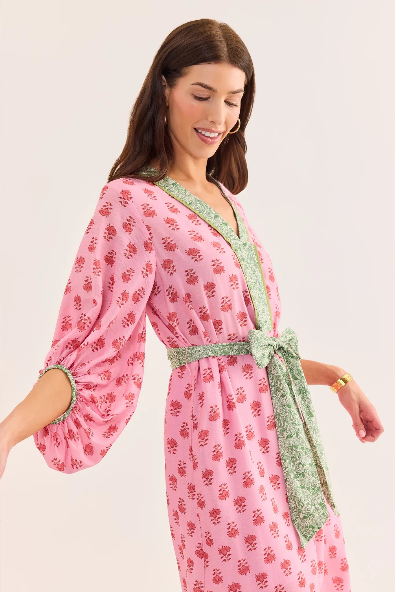 Woman wearing a pink floral dress with green trim on a white background standing