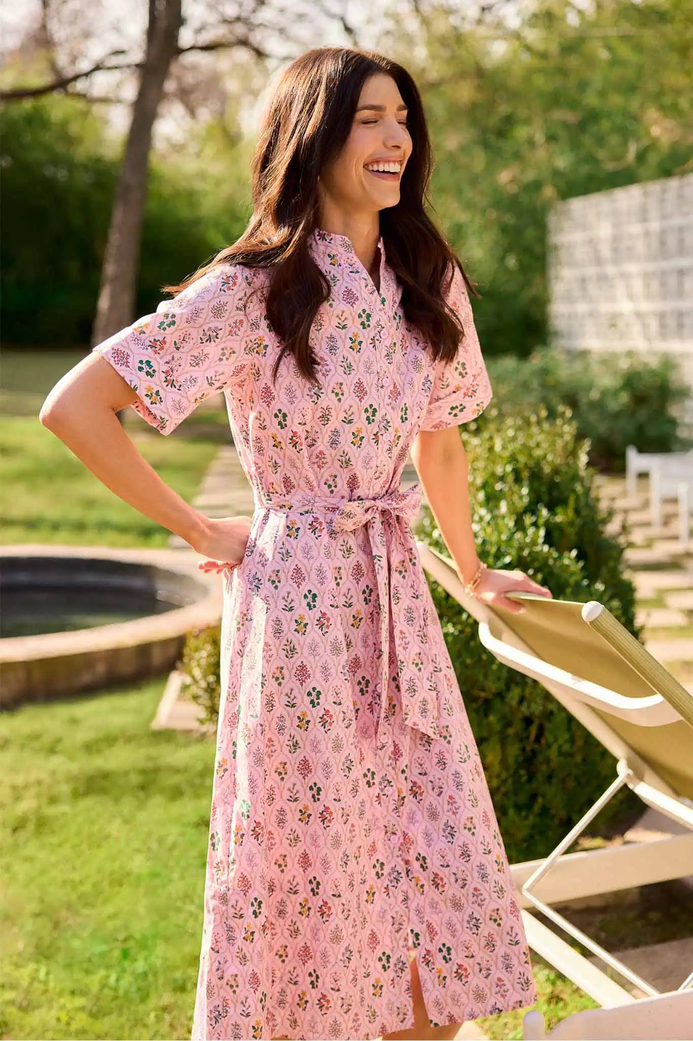 Woman in a pink floral dress standing outdoors in a garden.