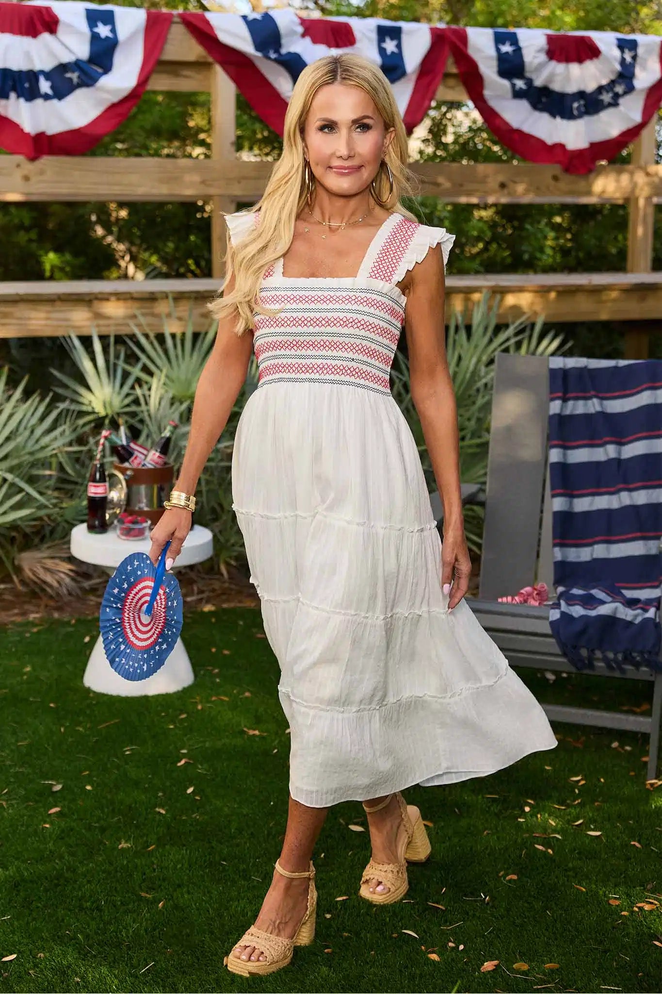 Woman in a red, white, and blue outfit with a white skirt standing outdoors with American flag decorations.