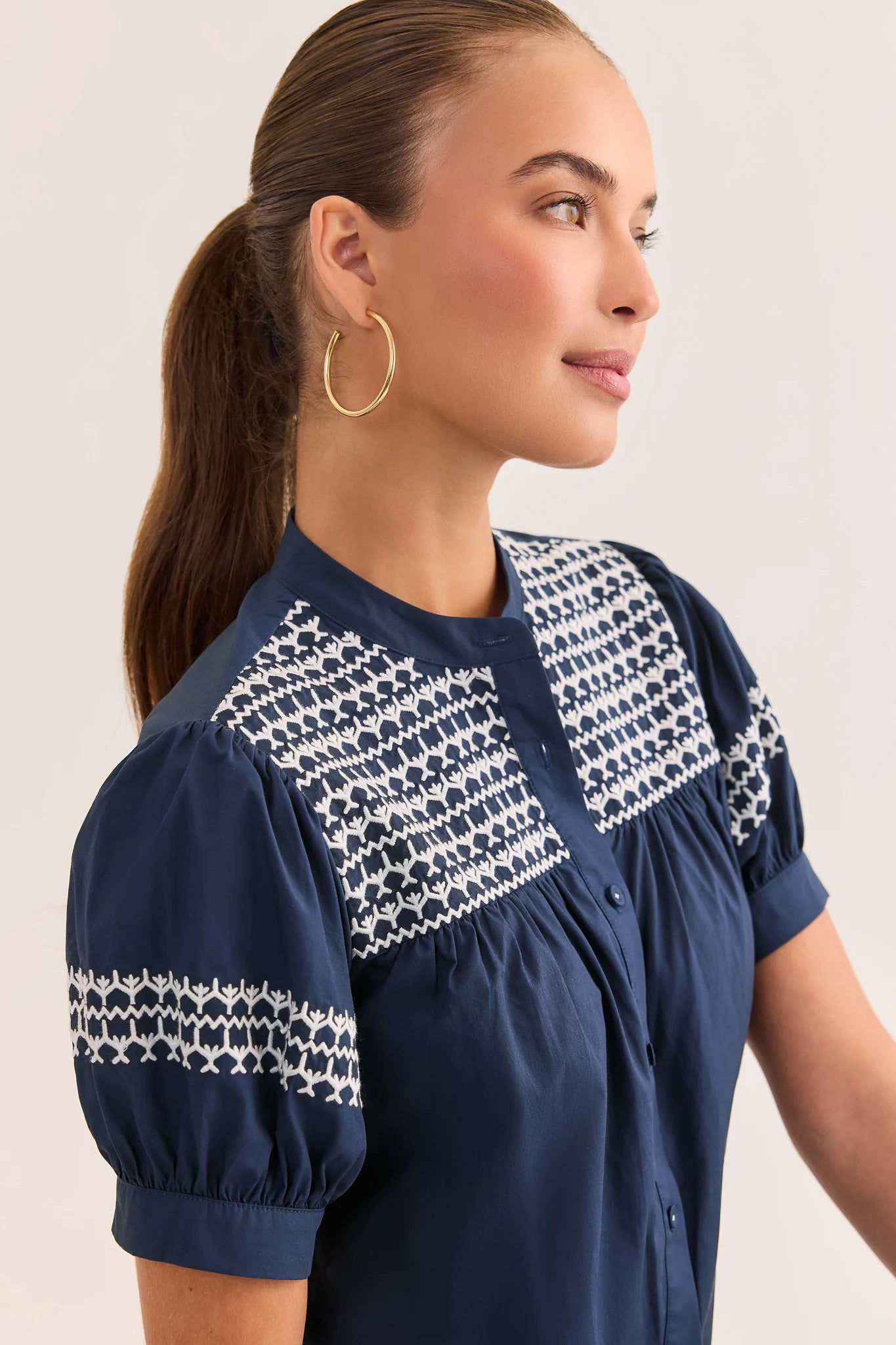 close up Woman wearing a navy blue top with white patterned details on a plain background