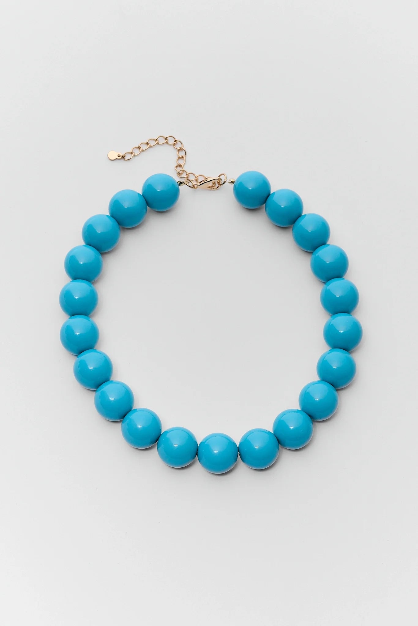 A beaded necklace with glossy turquoise blue round beads and a gold-tone chain extender, displayed on a light gray background.