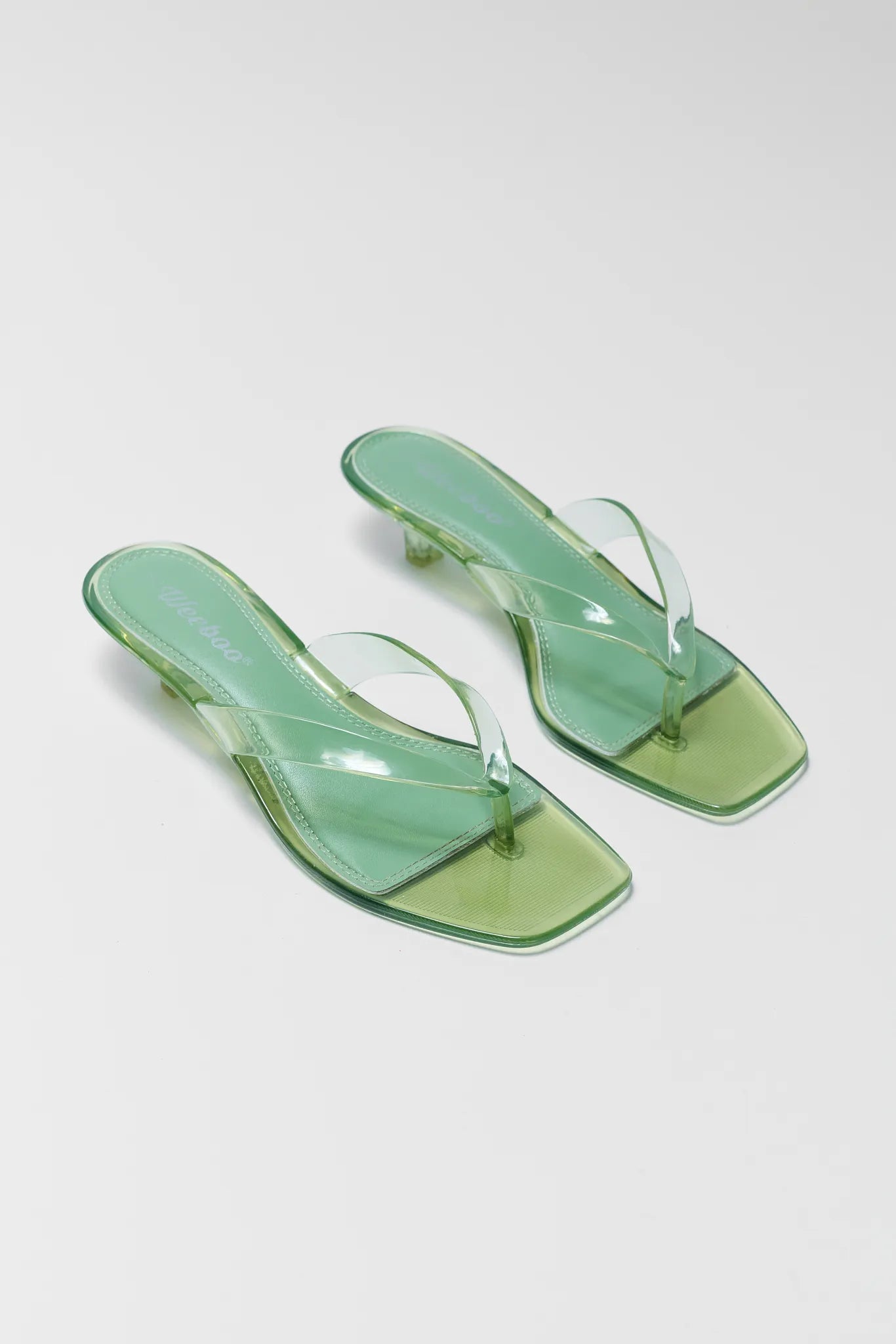 Pair of green transparent sandals on a light gray background