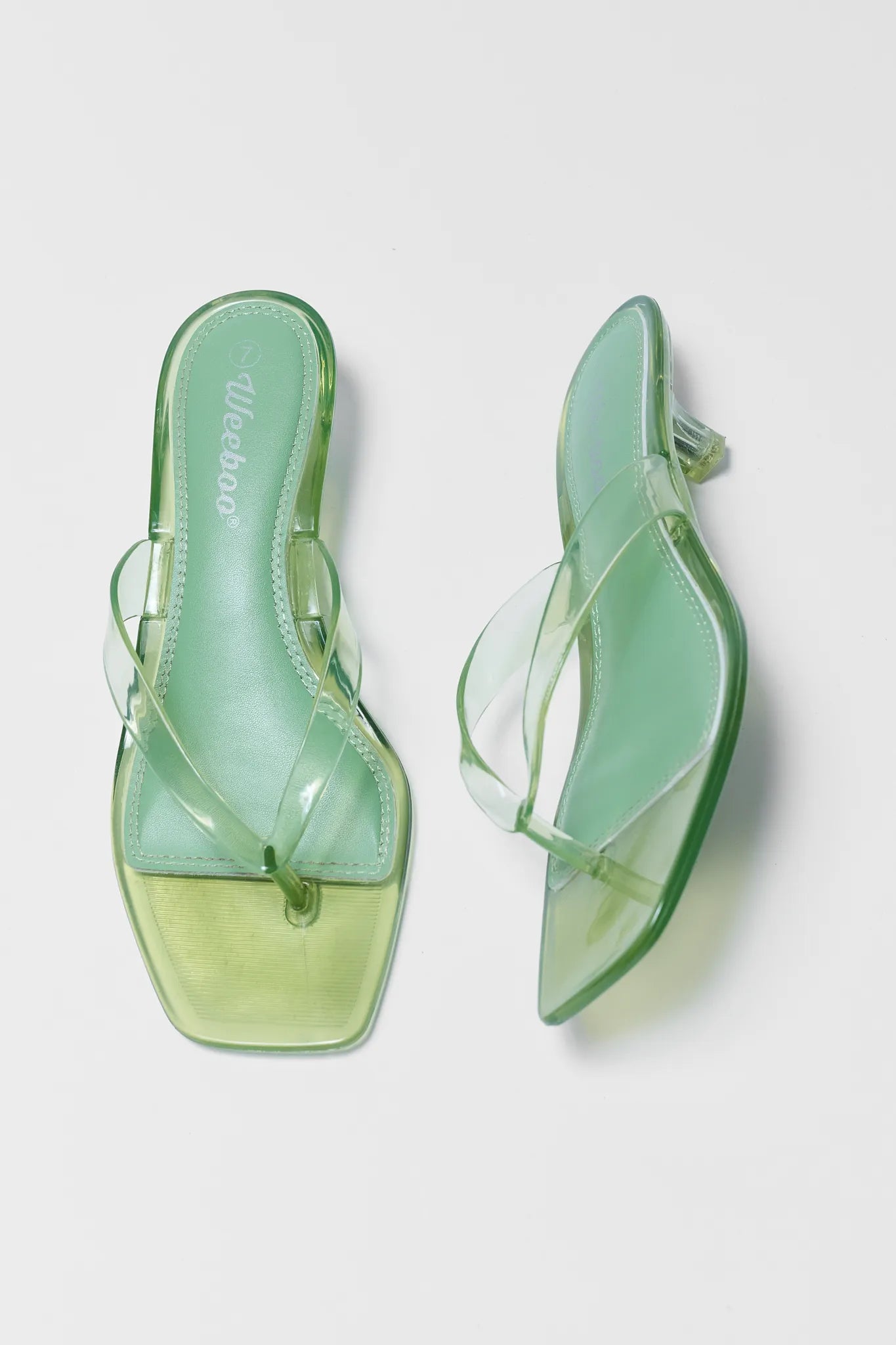 Pair of green transparent sandals on a light gray background