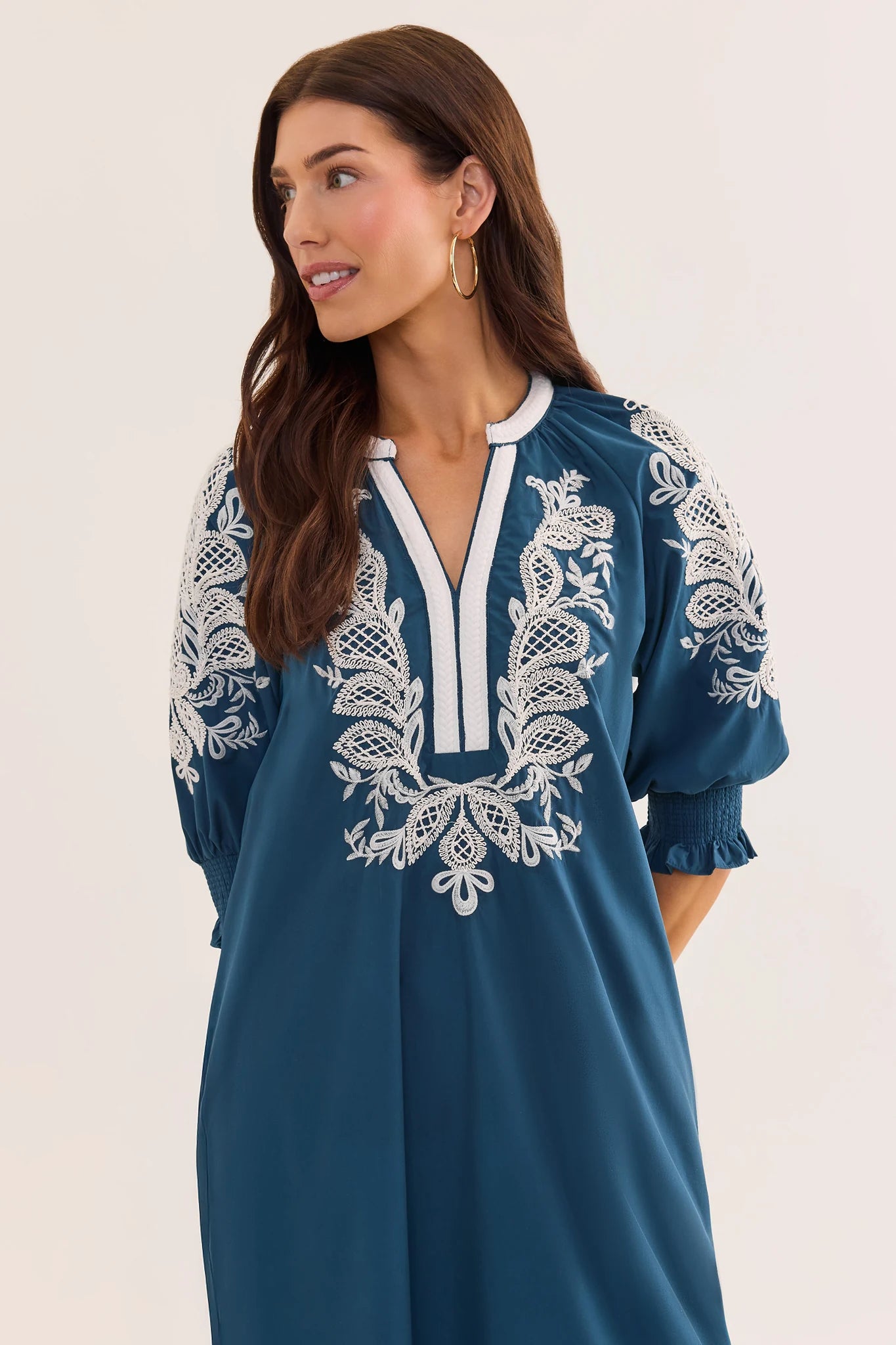 close up Woman wearing a blue dress with white embroidery on a plain background