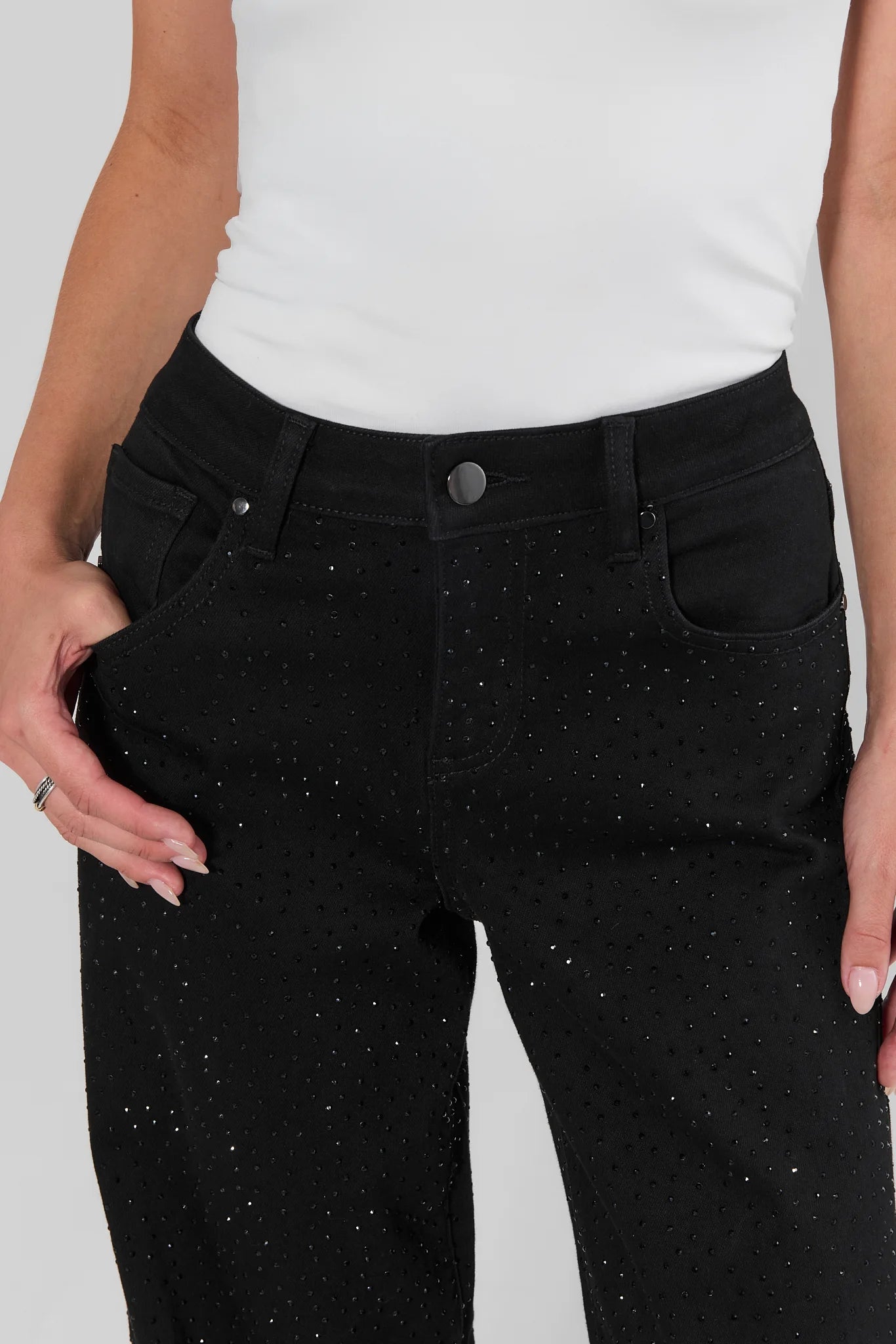 Black denim jeans with a perforated dot pattern and subtle silver glitter flecks, shown on a model wearing a white top against a light gray background. close up