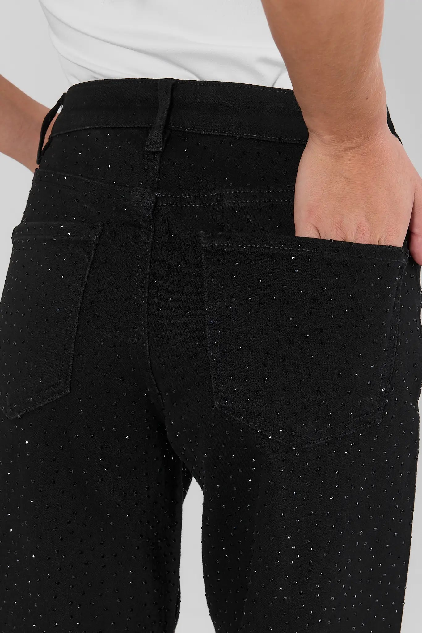 Close-up of a person wearing black jeans with a subtle speckled texture, showing the back pocket and waistband.