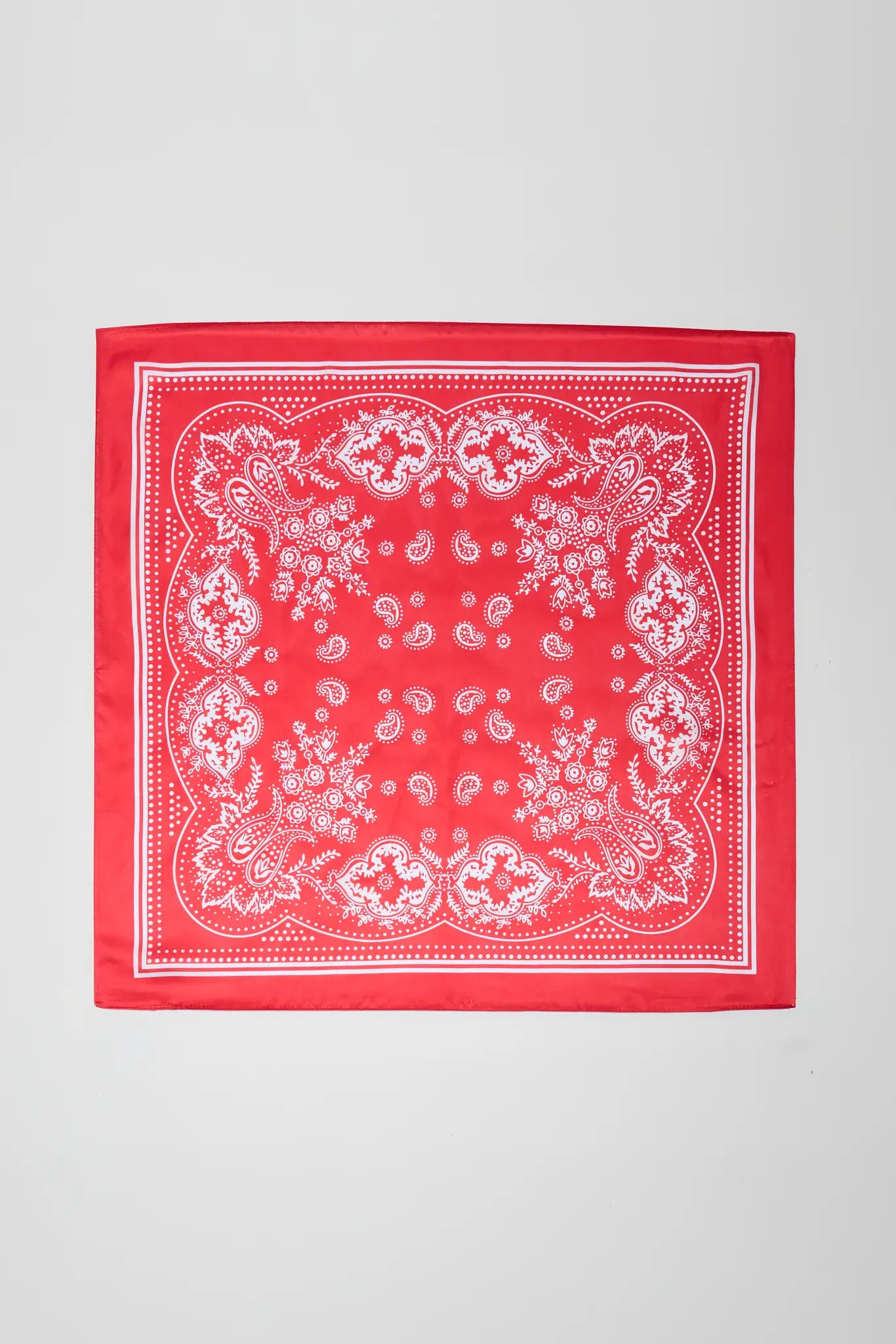A square red bandana with a white paisley pattern, laid flat against a light gray background.