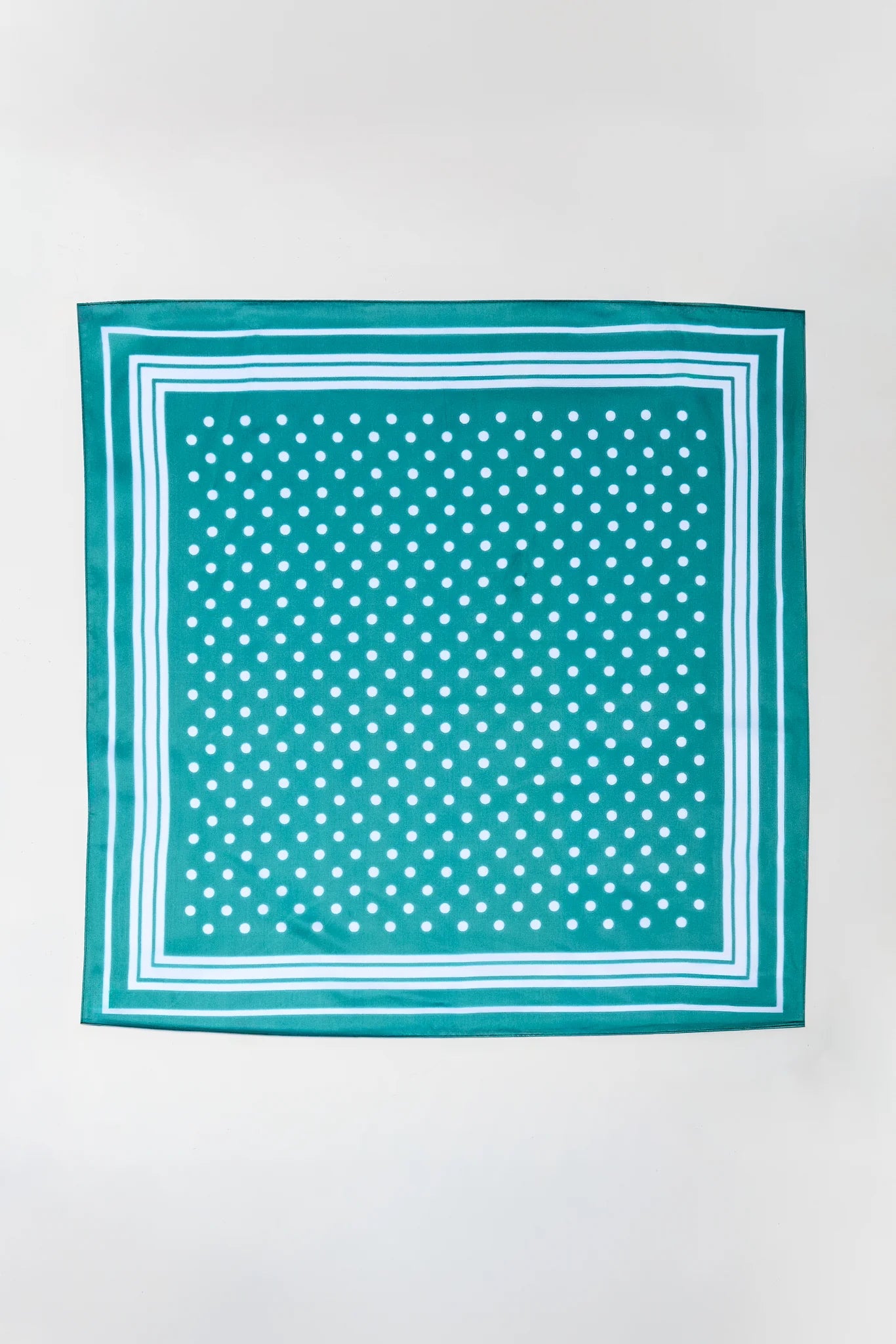 A square scarf with a teal green body, featuring a white polka dot pattern in the center and a double white border, laid flat against a light gray background.