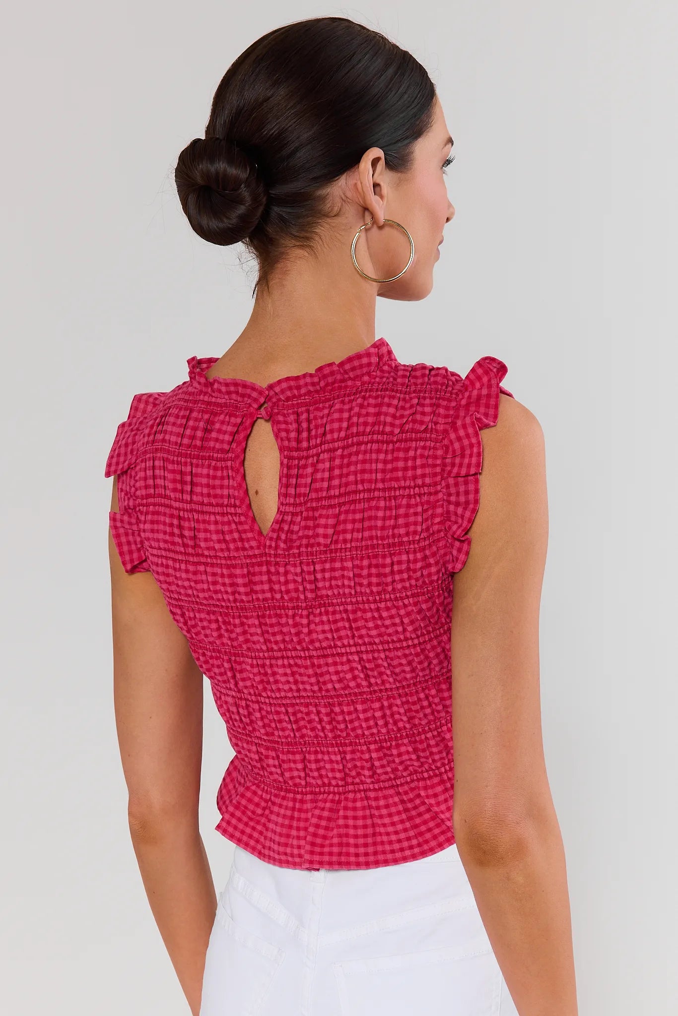 Woman standing wearing a pink textured top with ruffled shoulders on a white background