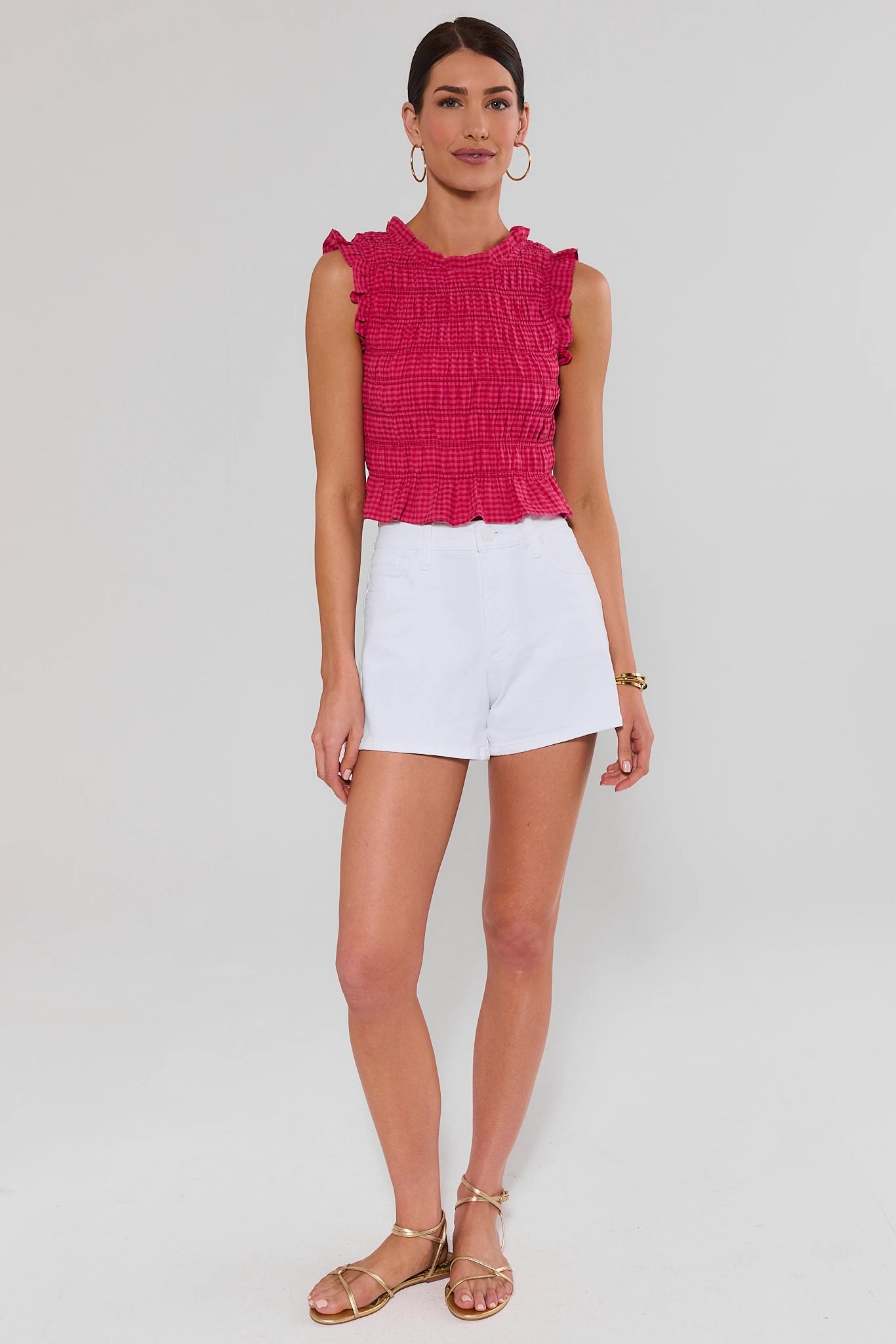 Woman wearing a pink ruffled top and white shorts on a light gray background