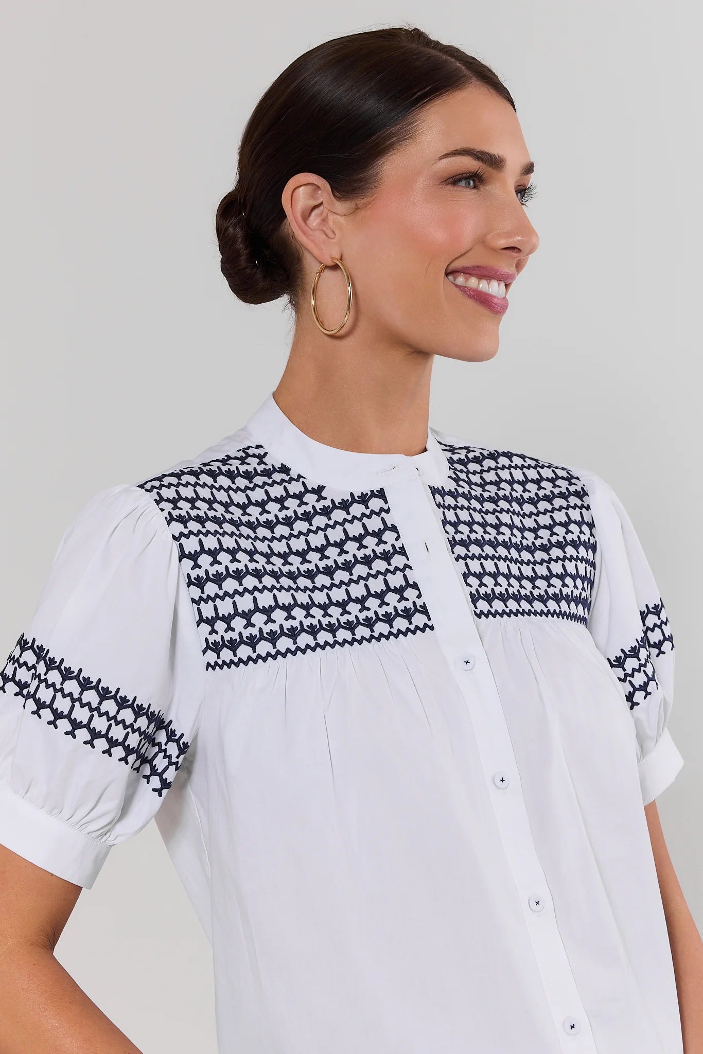close up Woman wearing a white blouse with black geometric patterns on a plain background