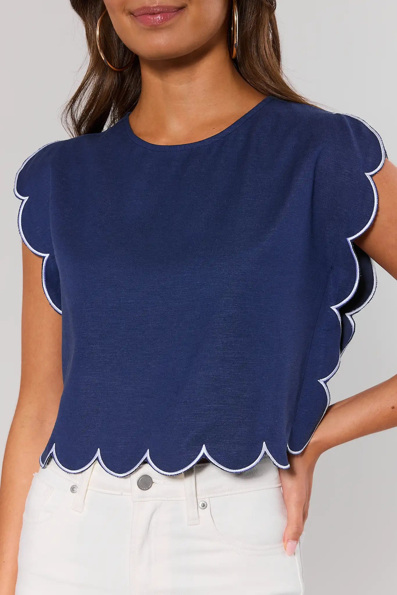 close up Woman wearing a navy blue top with scalloped edges on a plain background