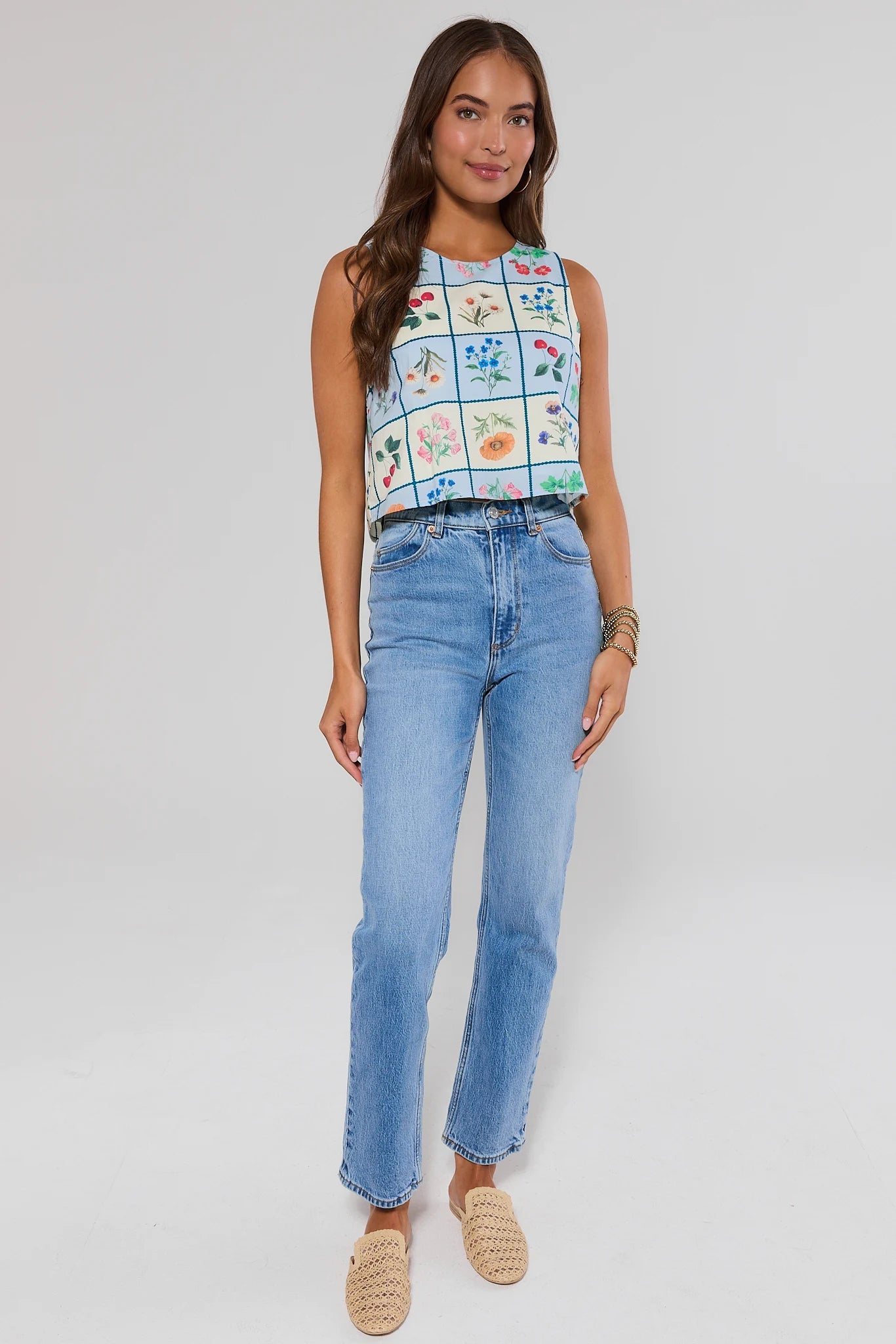 Woman wearing a sleeveless top with a floral pattern and blue jeans on a white background
