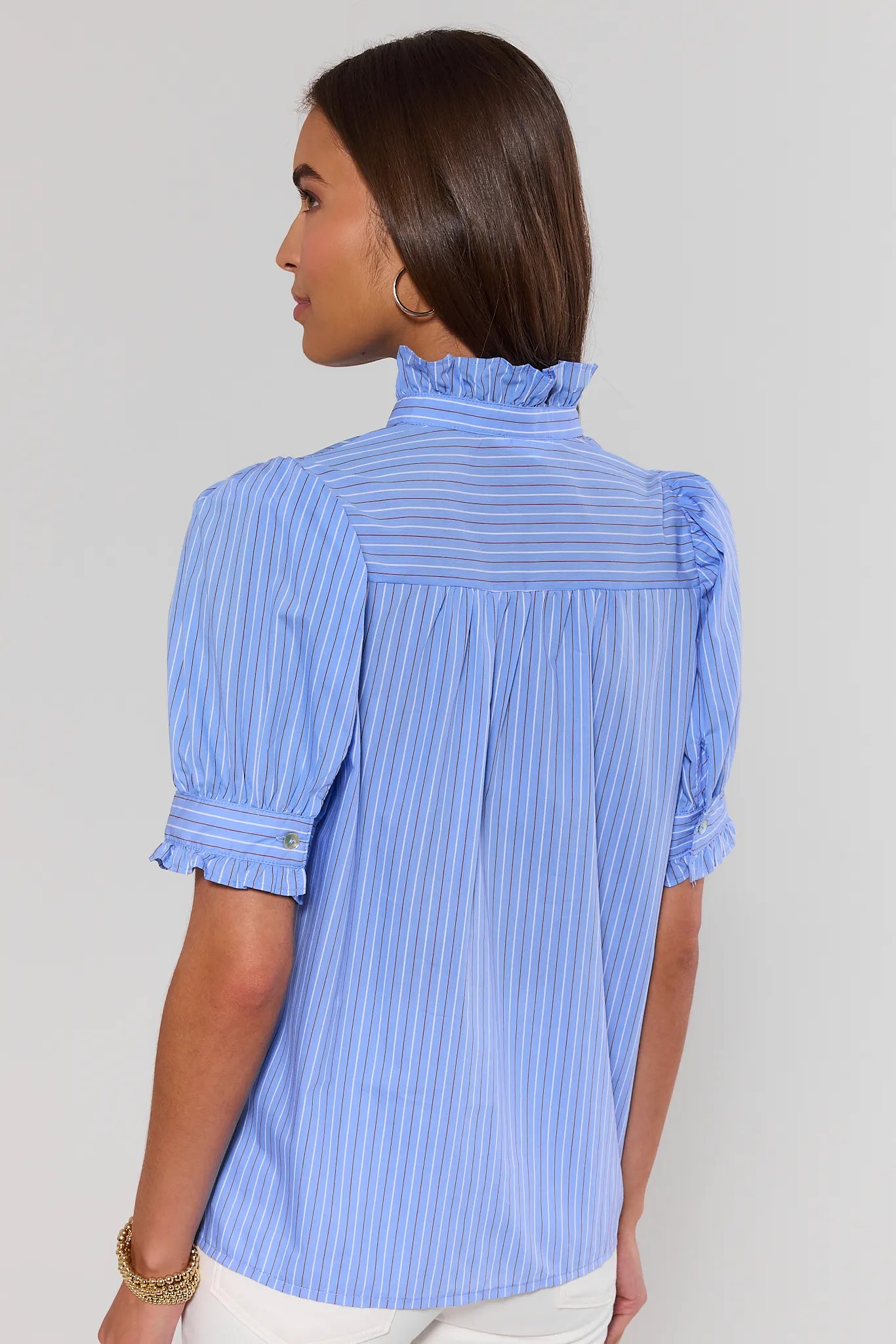 Woman standing wearing a blue striped blouse with ruffled shoulders on a plain background