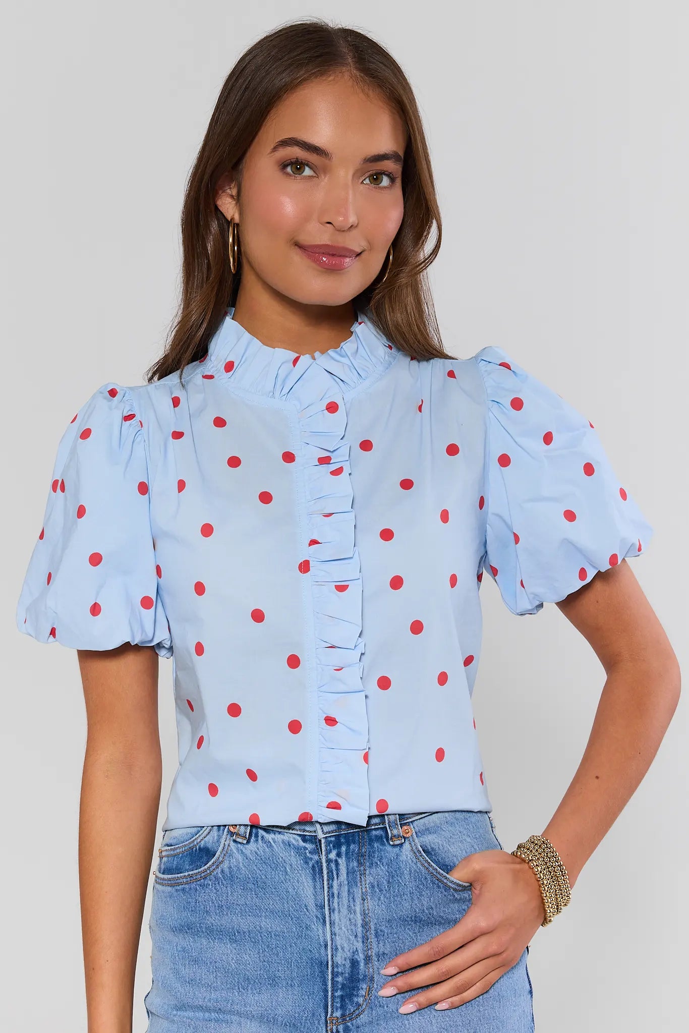 Woman wearing a light blue blouse with red polka dots and jeans on a plain background