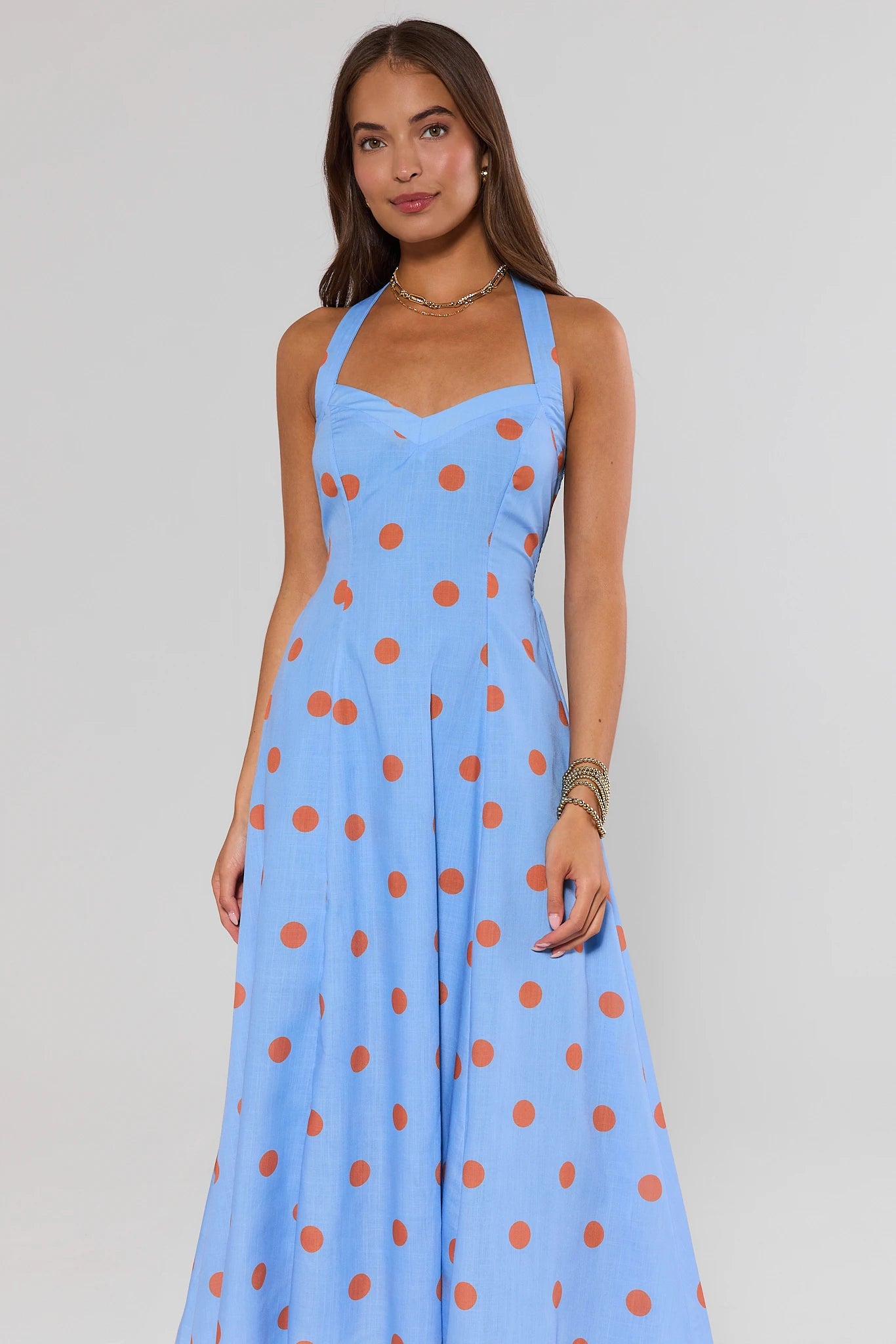 Woman wearing a blue dress with orange polka dots against a plain background