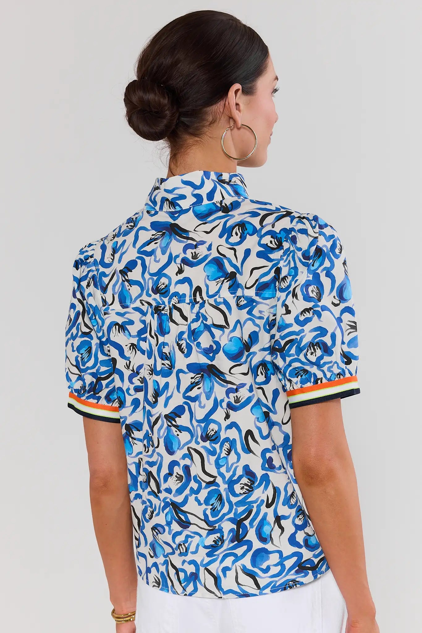 Woman standing wearing a blue and white patterned shirt on a plain background