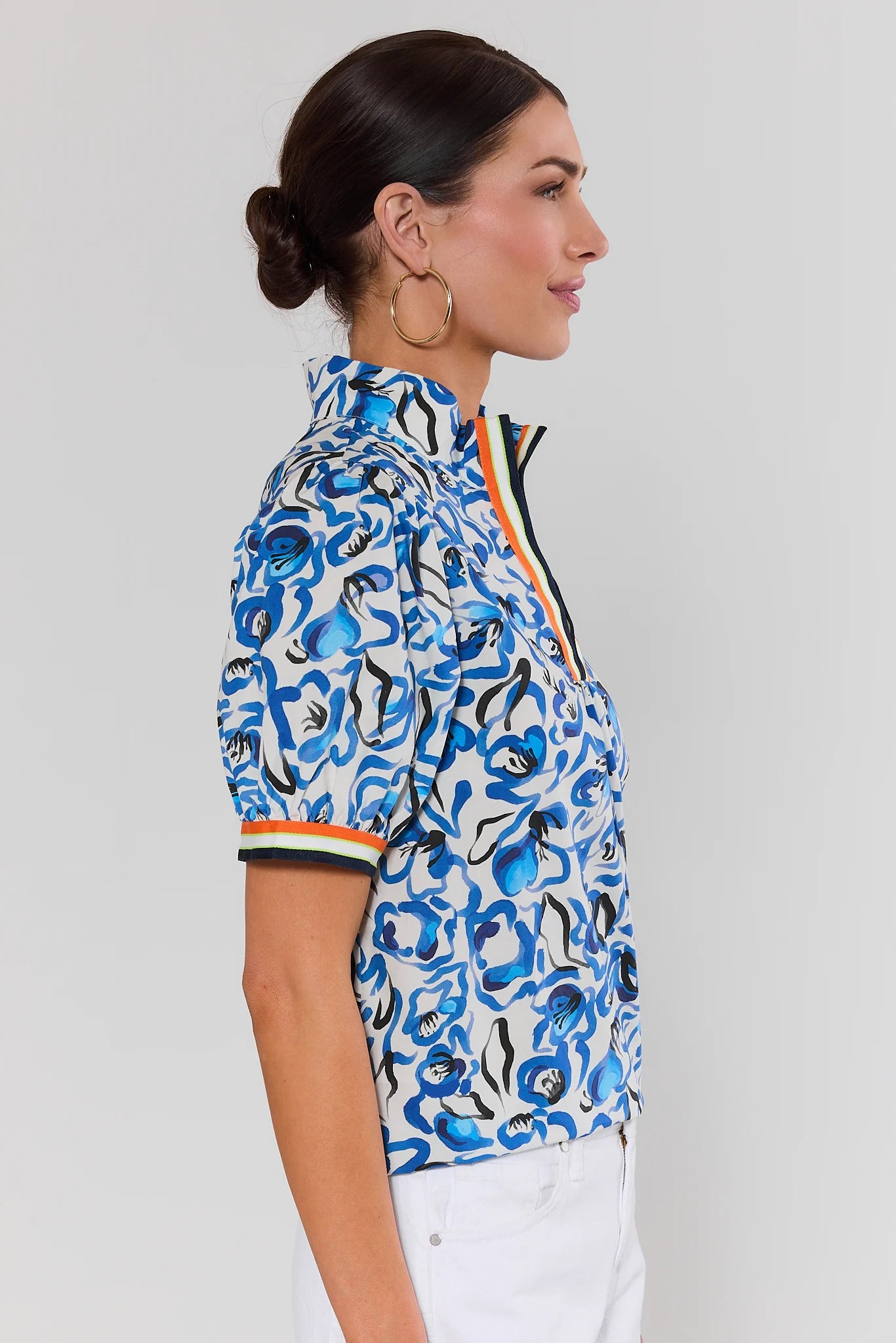 side shot Woman wearing a blue patterned shirt with white pants on a gray background