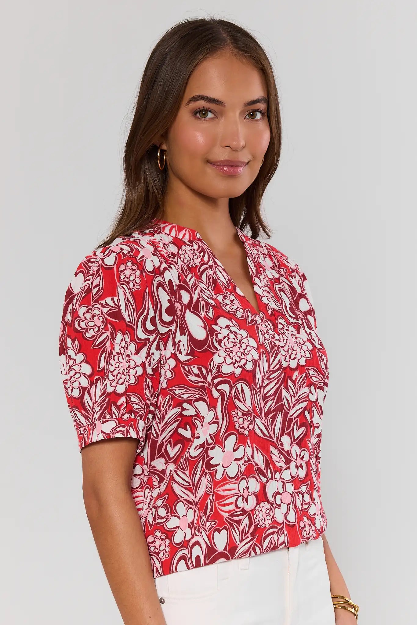 side shot Woman wearing a red floral blouse against a plain background
