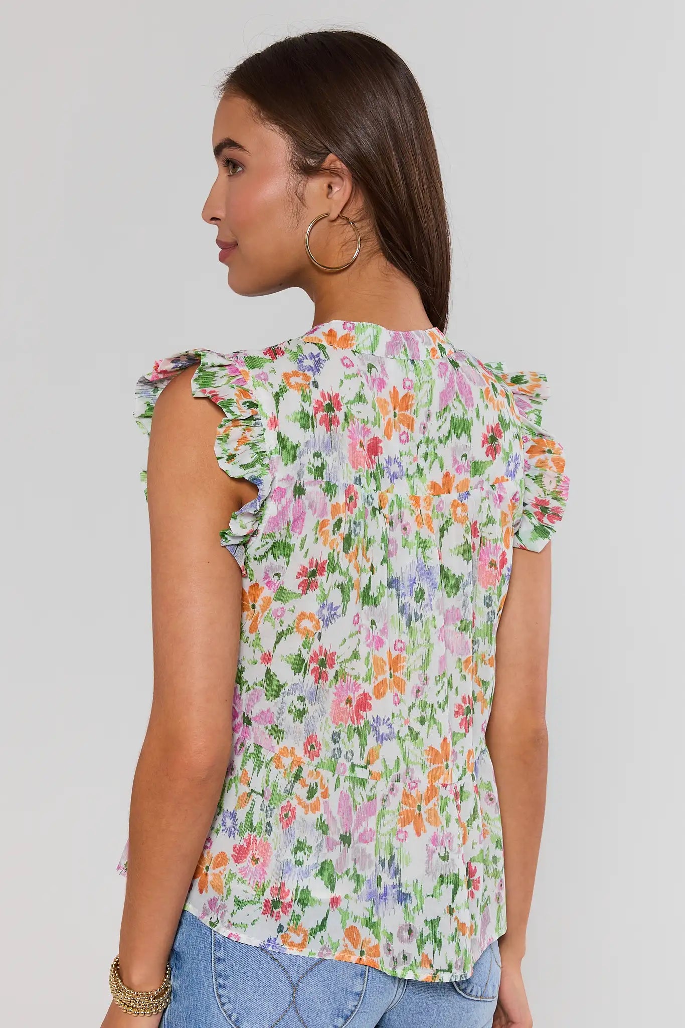 Woman wearing a floral blouse with ruffled sleeves on a plain background standing