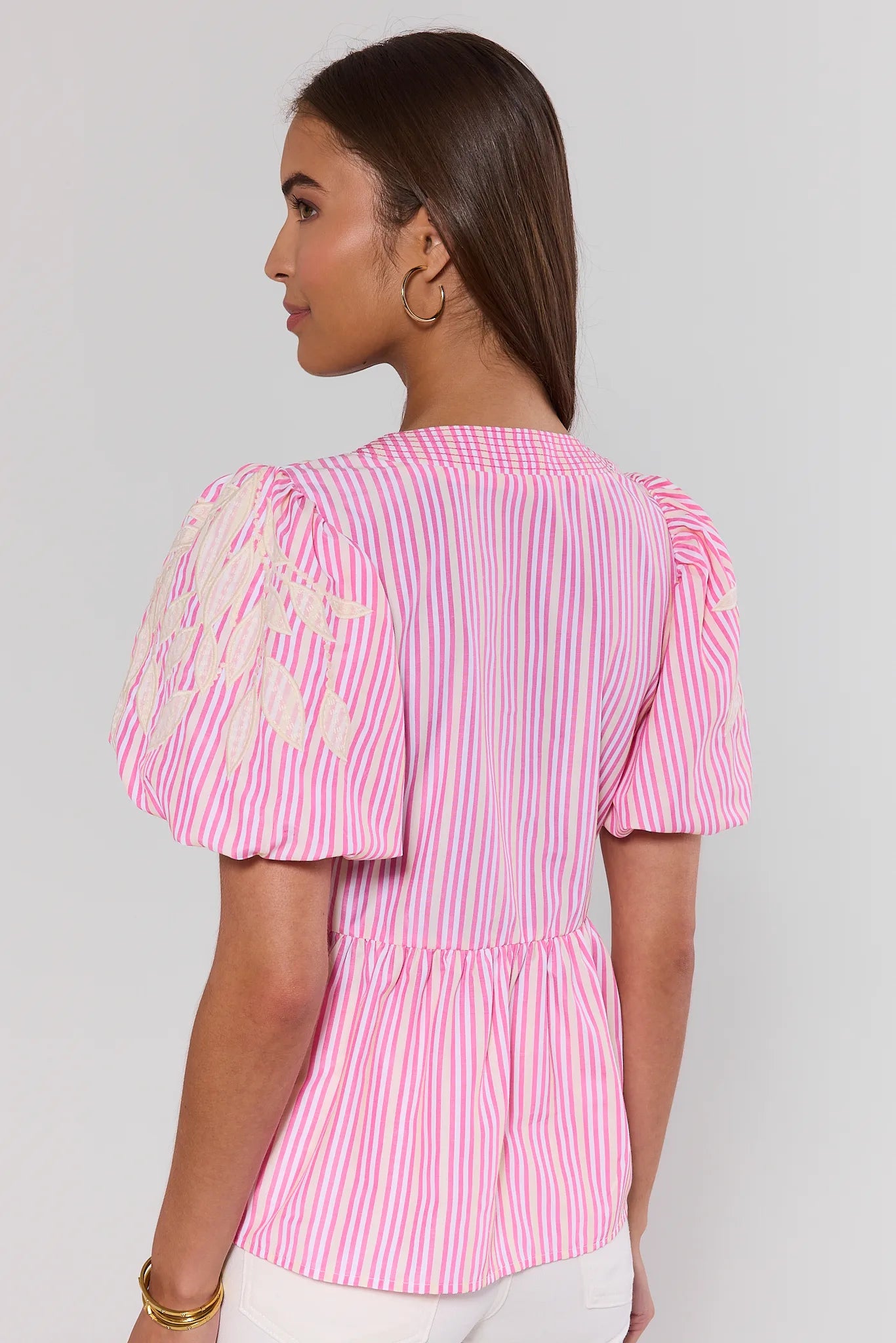 Woman standing wearing a pink and white striped blouse with ruffled sleeves on a plain background