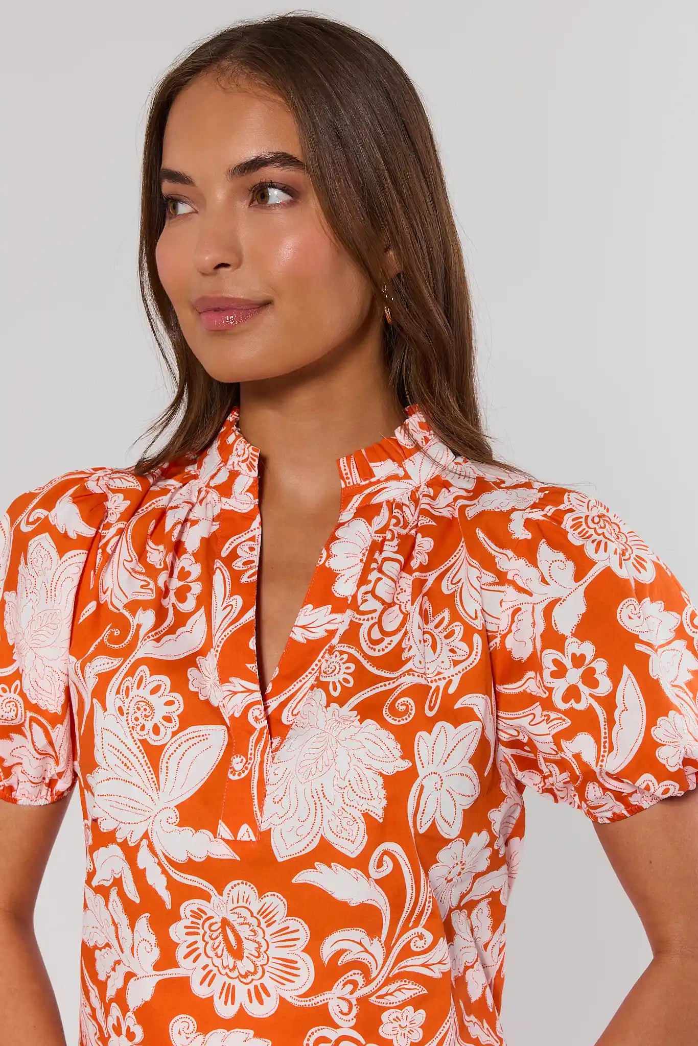 close up Woman wearing an orange and white floral patterned shirt against a plain background