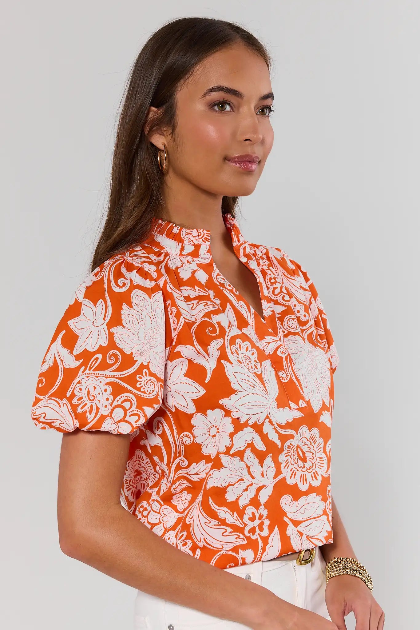 side shot Woman wearing an orange floral blouse against a plain background