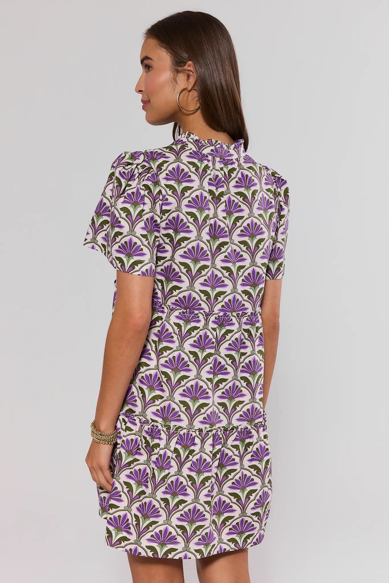Woman standing wearing a purple and green patterned dress on a plain background