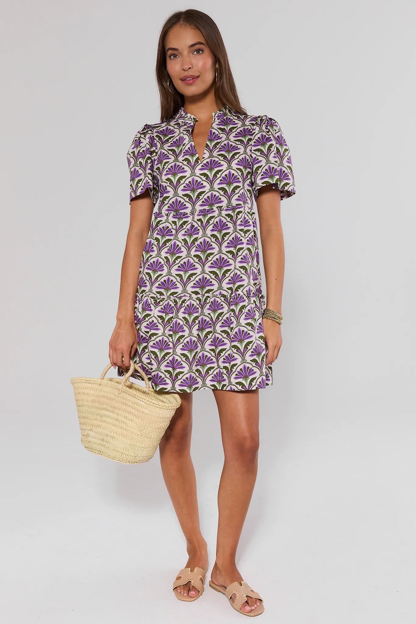 Woman wearing a purple floral dress holding a straw bag on a white background