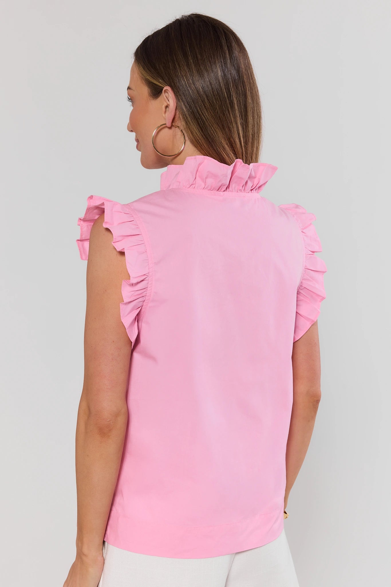 Woman standing wearing a pink sleeveless top with ruffled shoulders against a plain background