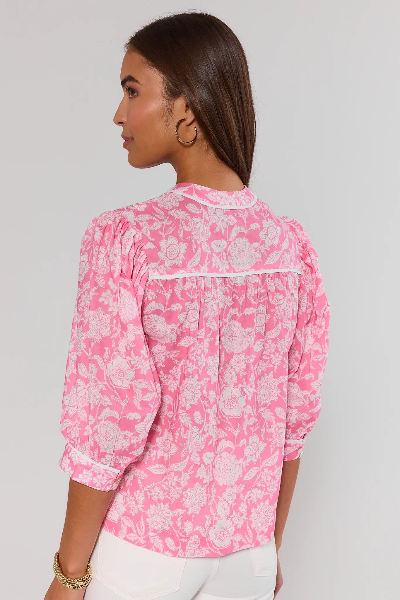 Woman standing wearing a pink floral blouse against a plain background